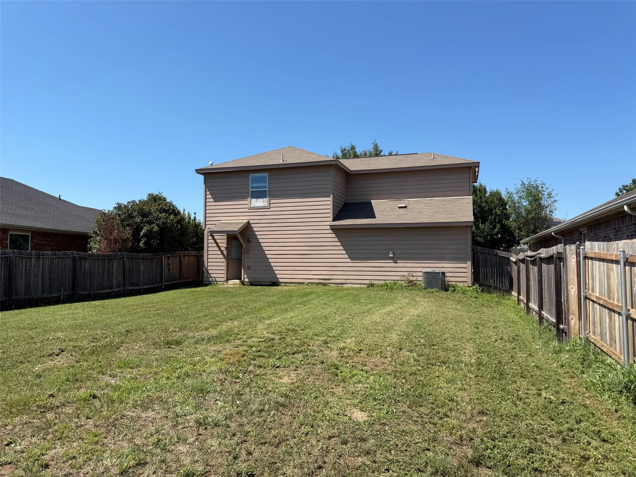 Expansive backyard featuring a large grass lawn, perimeter wood fencing, and a two-story home with tan siding