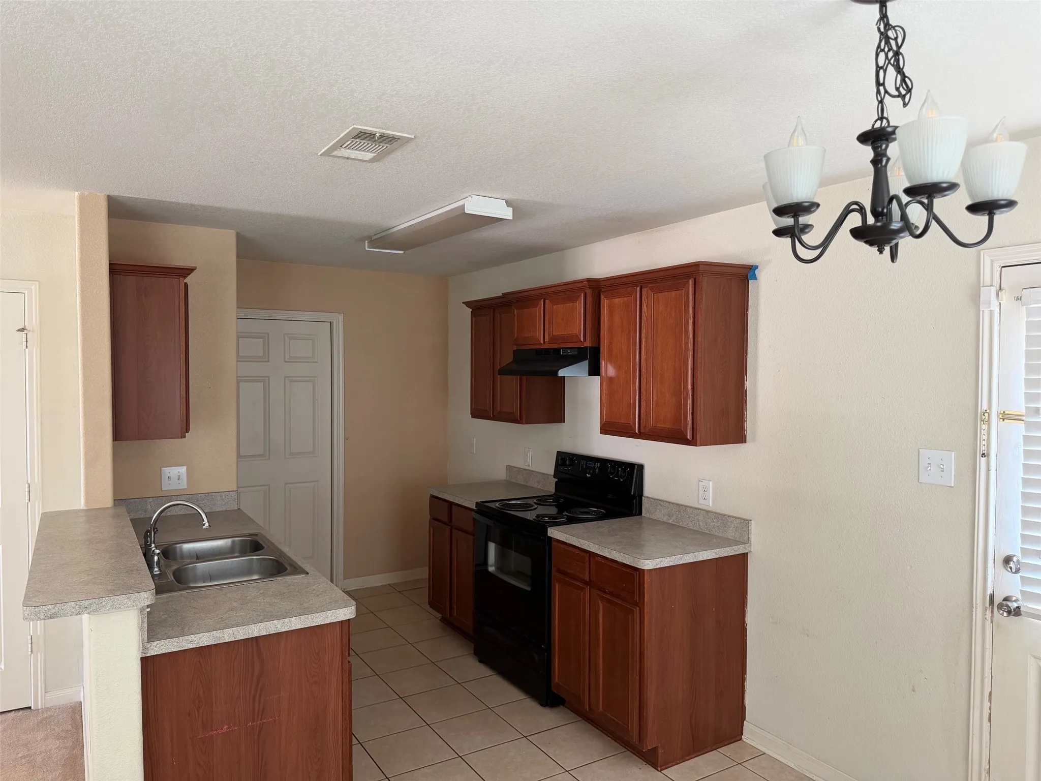 Kitchen featuring wood-finish cabinetry, a double basin stainless steel sink, and light-toned countertops
