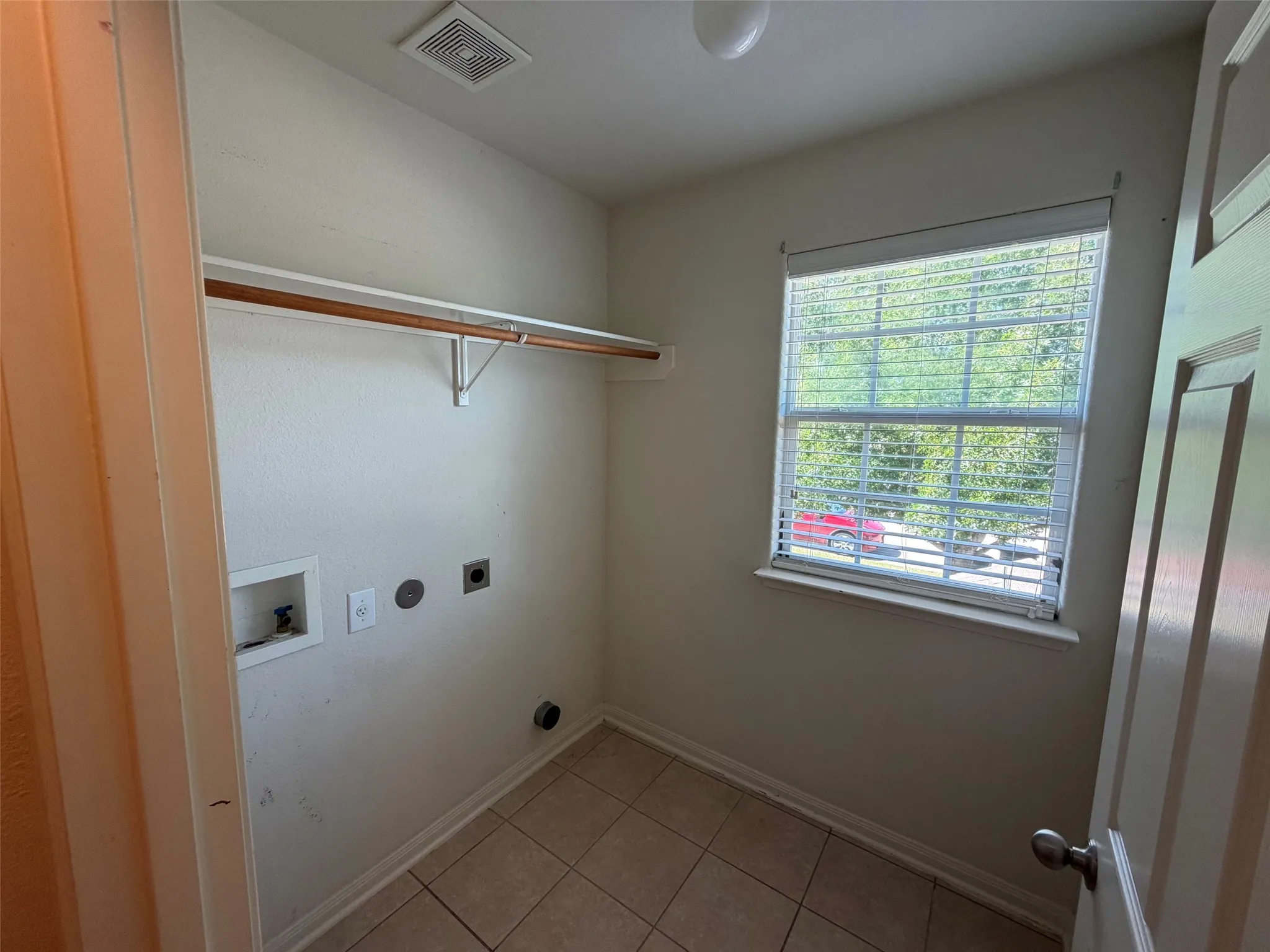 Laundry area featuring tile flooring, a single window with blinds, and a built-in hanging rod