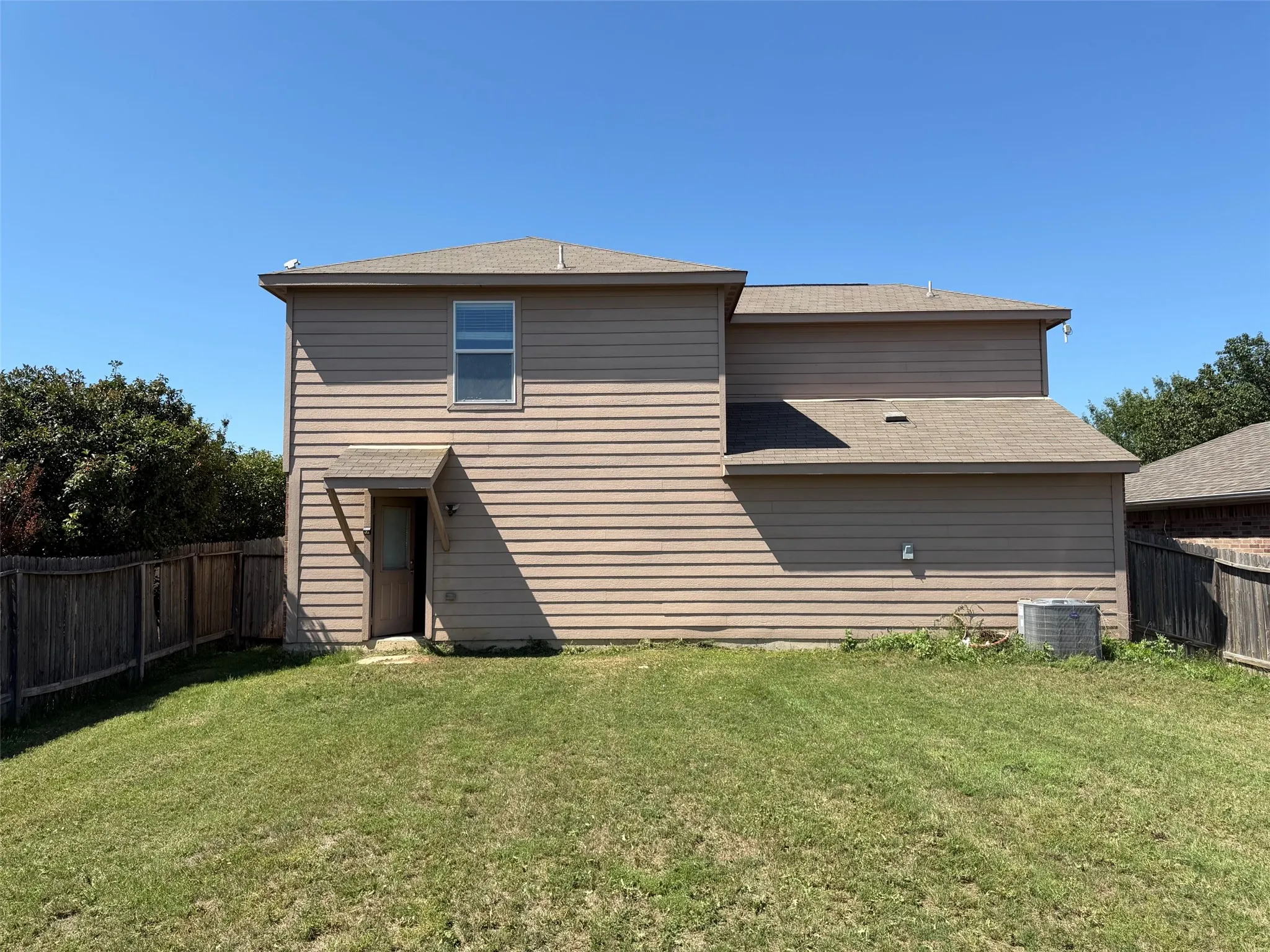 Two-story residence featuring tan siding and a fenced backyard