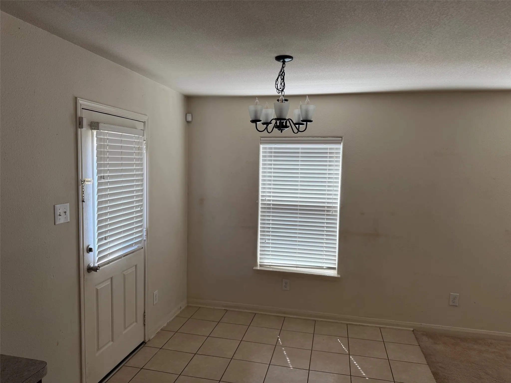Dining area featuring a three-panel door with integrated blinds, a window with horizontal blinds, a ceiling-mounted chandelier, and ceramic tile flooring