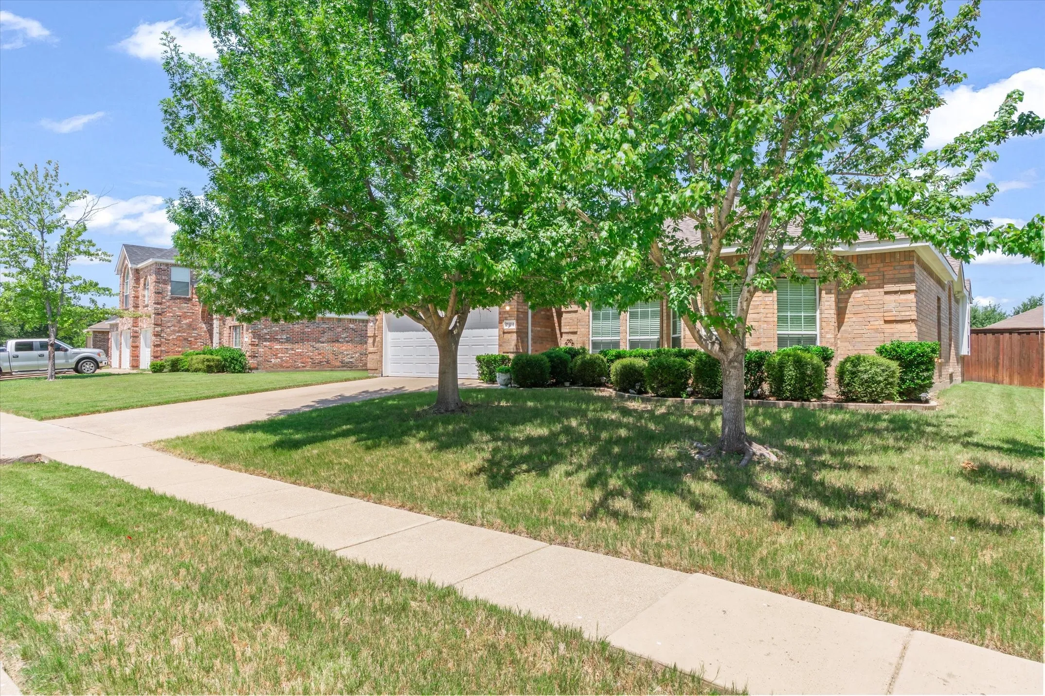 Traditional brick-veneer exterior featuring multiple windows, an attached garage, a concrete driveway, and a sidewalk