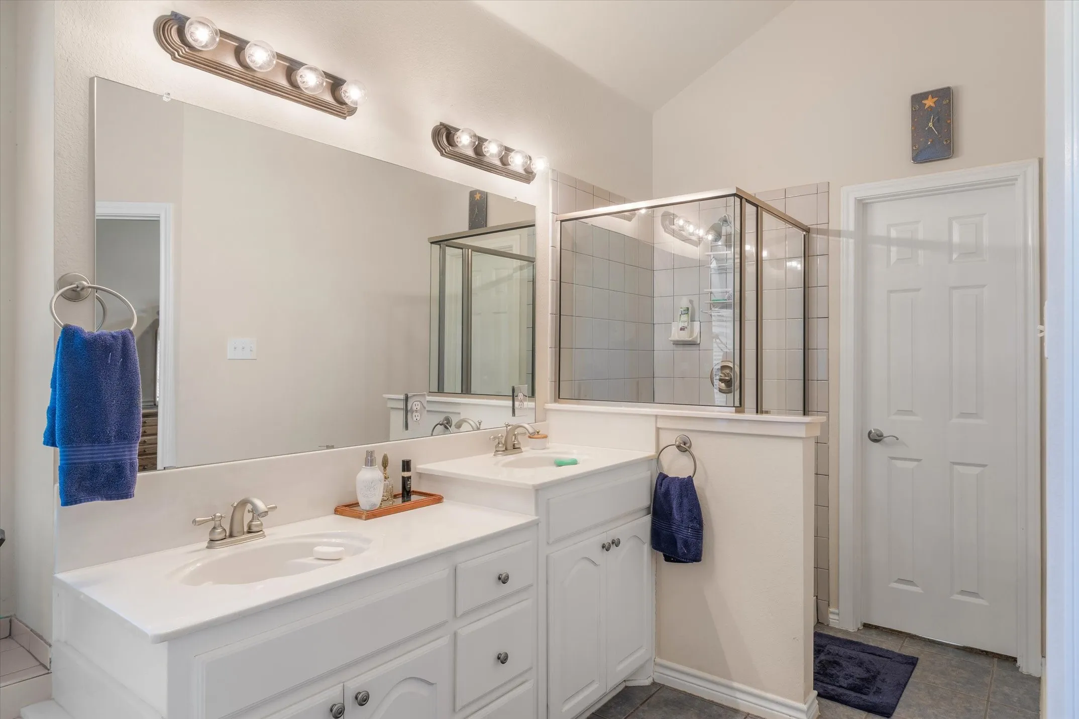 Bathroom featuring a double vanity with white cabinetry and integrated sinks, a large wall-mounted mirror, and overhead vanity lighting