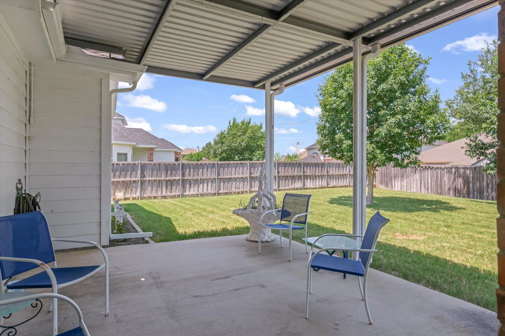Covered patio with a concrete slab, supporting metal posts, and a full corrugated metal roof