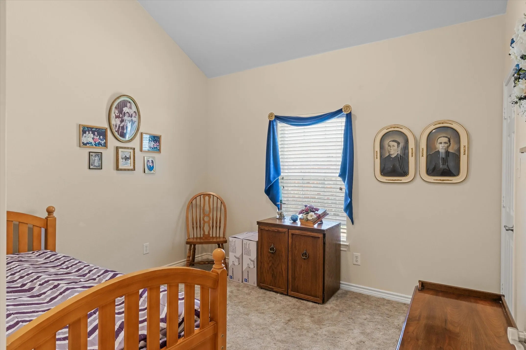 Vaulted ceiling room featuring neutral-toned walls, a window with horizontal blinds, and carpeting