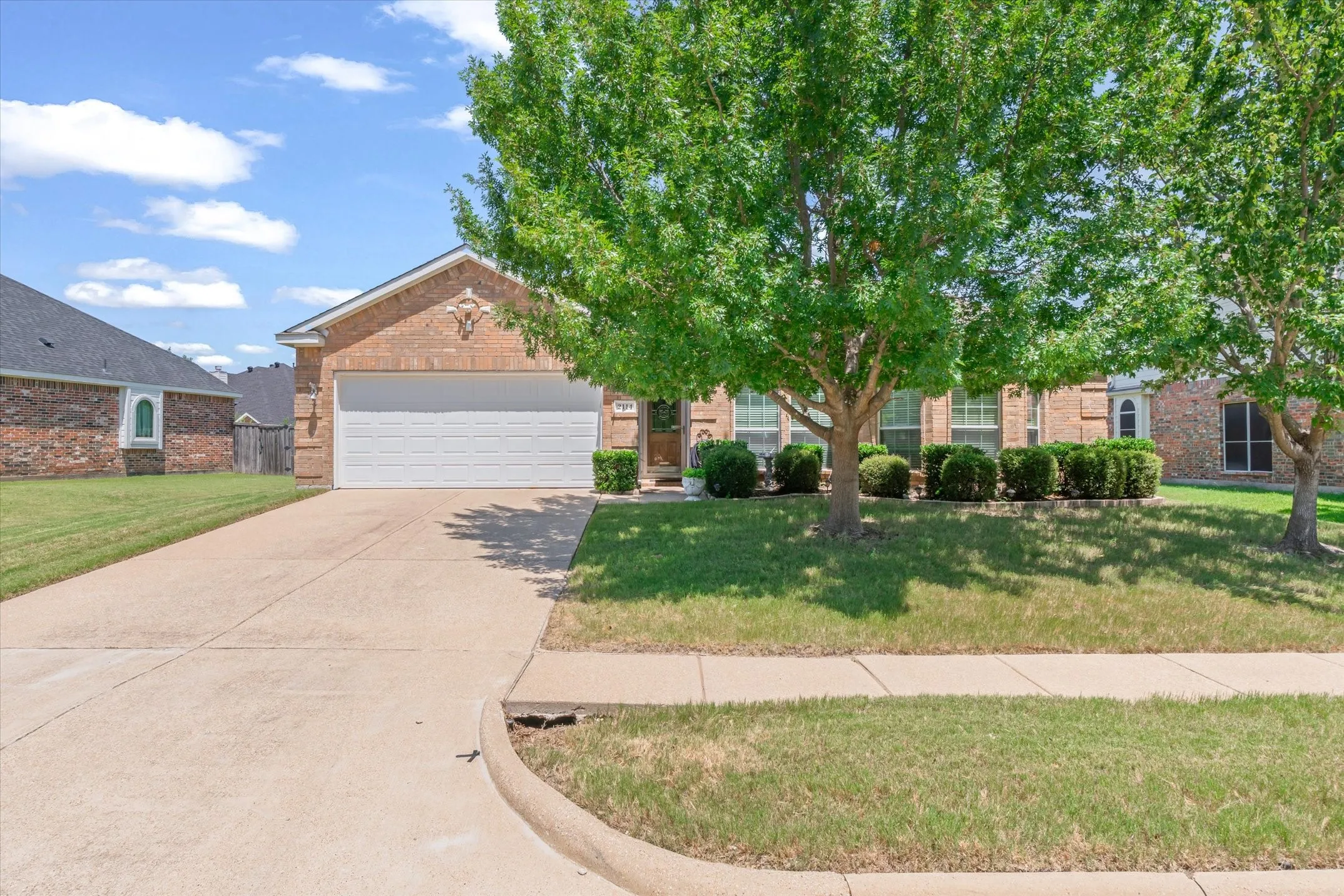 Brick exterior residence featuring a front-facing garage, concrete driveway, and mature landscaping