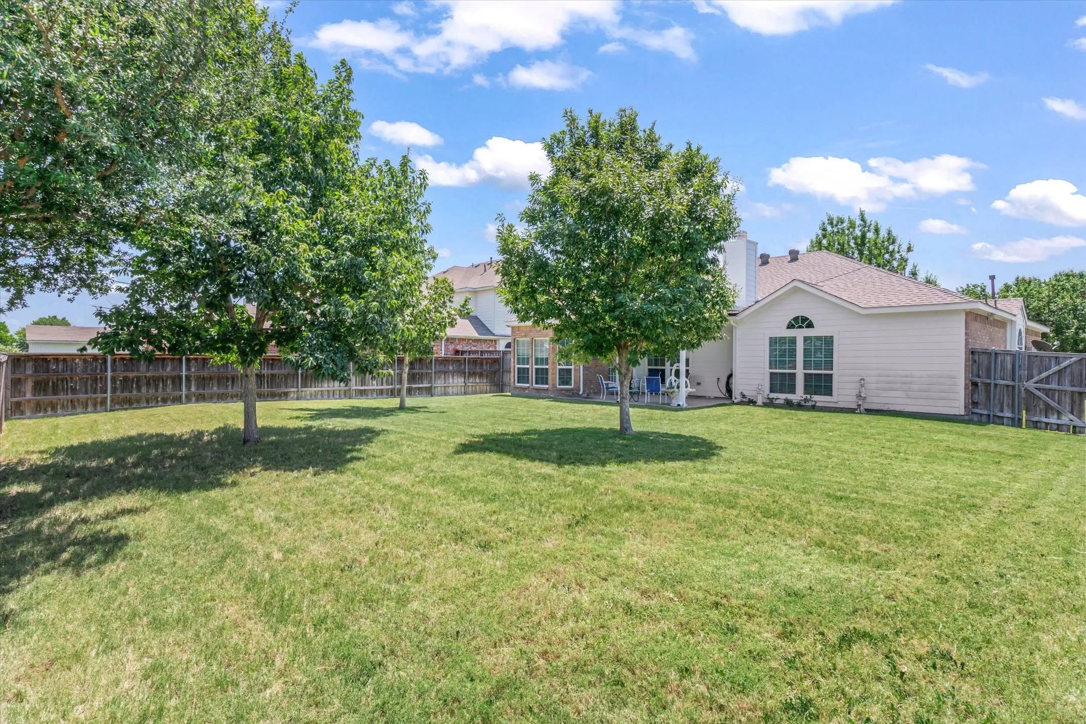 Expansive lawn with mature trees and wood fencing, offering a private outdoor environment