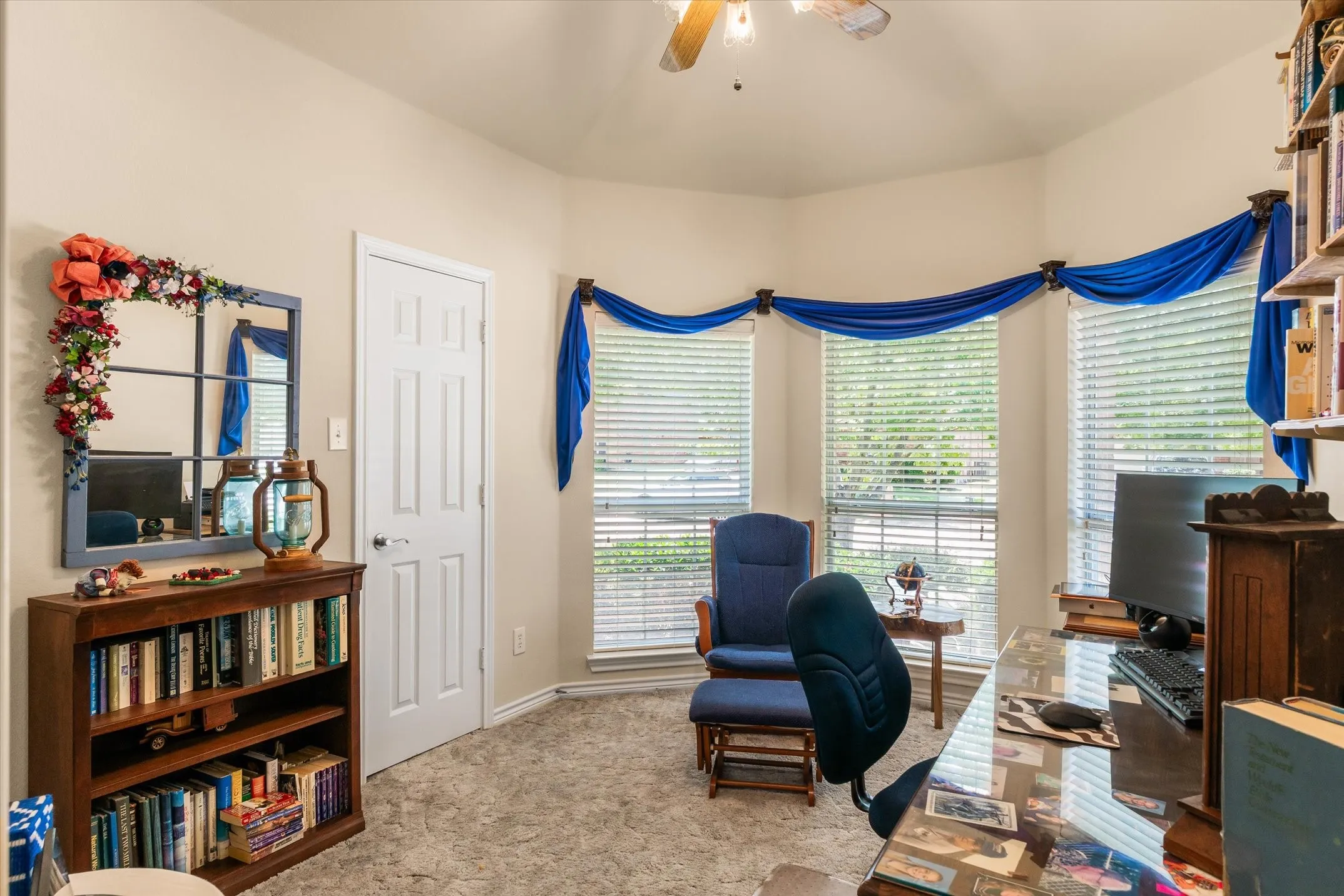 Bay window with multiple window blinds, ceiling fan, and carpeted flooring