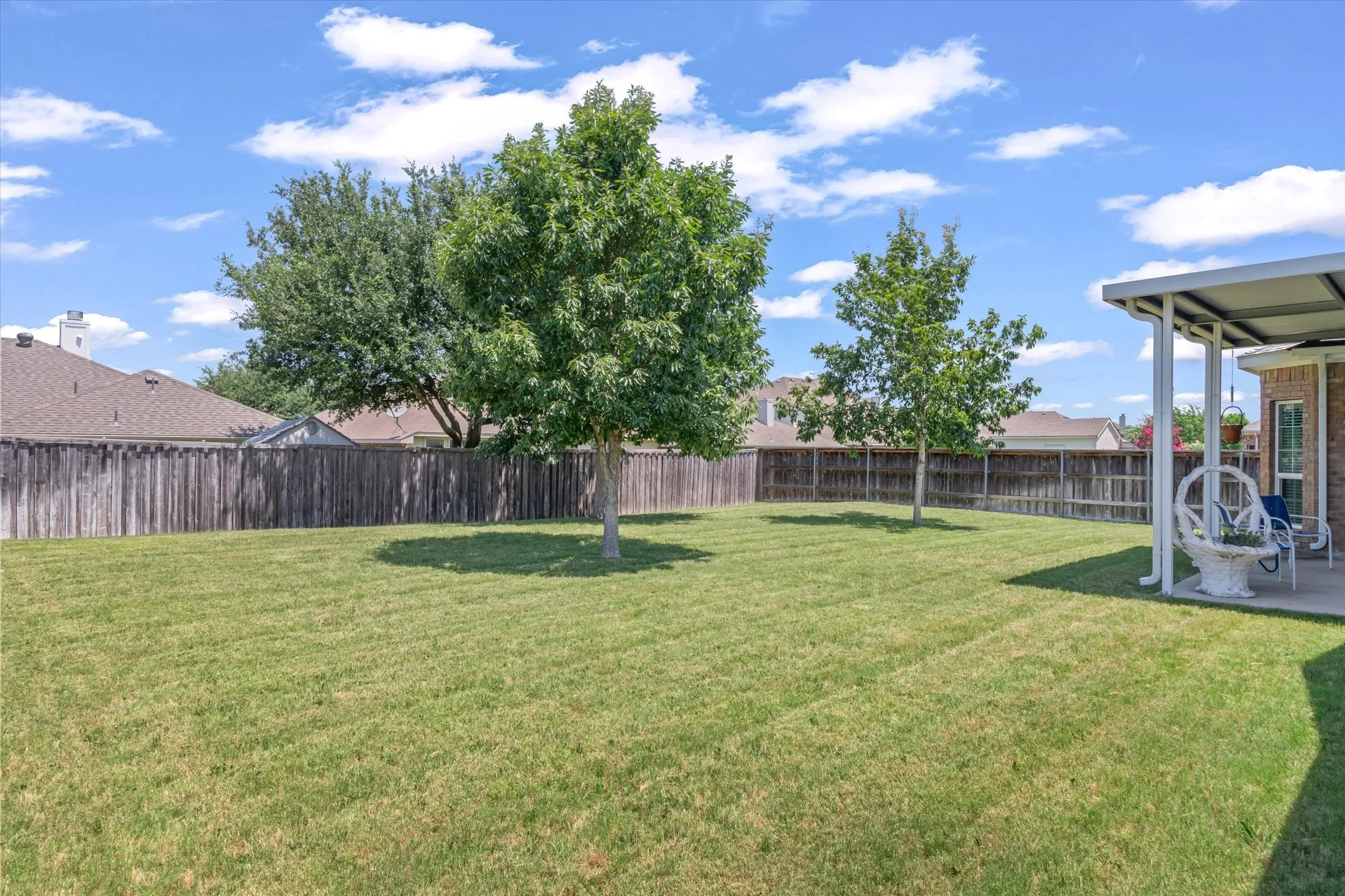 Expansive backyard featuring a manicured lawn, established trees, and a full privacy fence