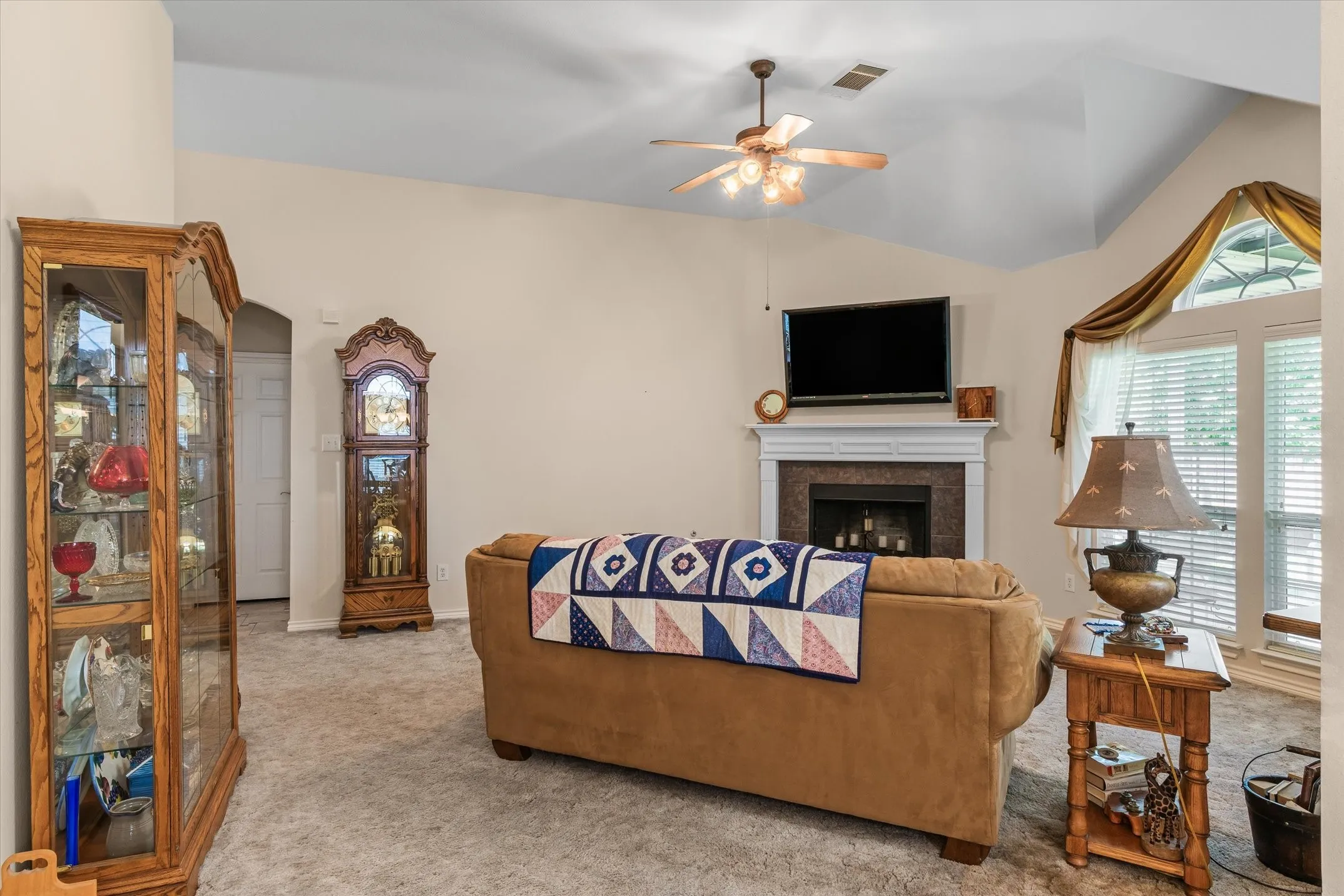 Living area featuring a vaulted ceiling with a ceiling fan, a fireplace with a white mantel and stone surround, and light-colored carpeting