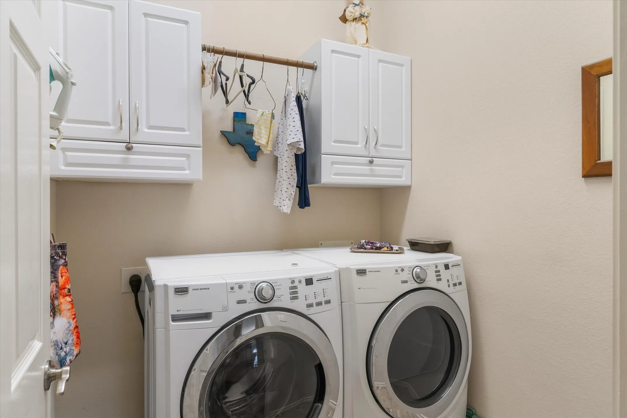 Dedicated laundry area featuring white shaker-style upper cabinetry, a built-in hanging rod, and light neutral wall paint