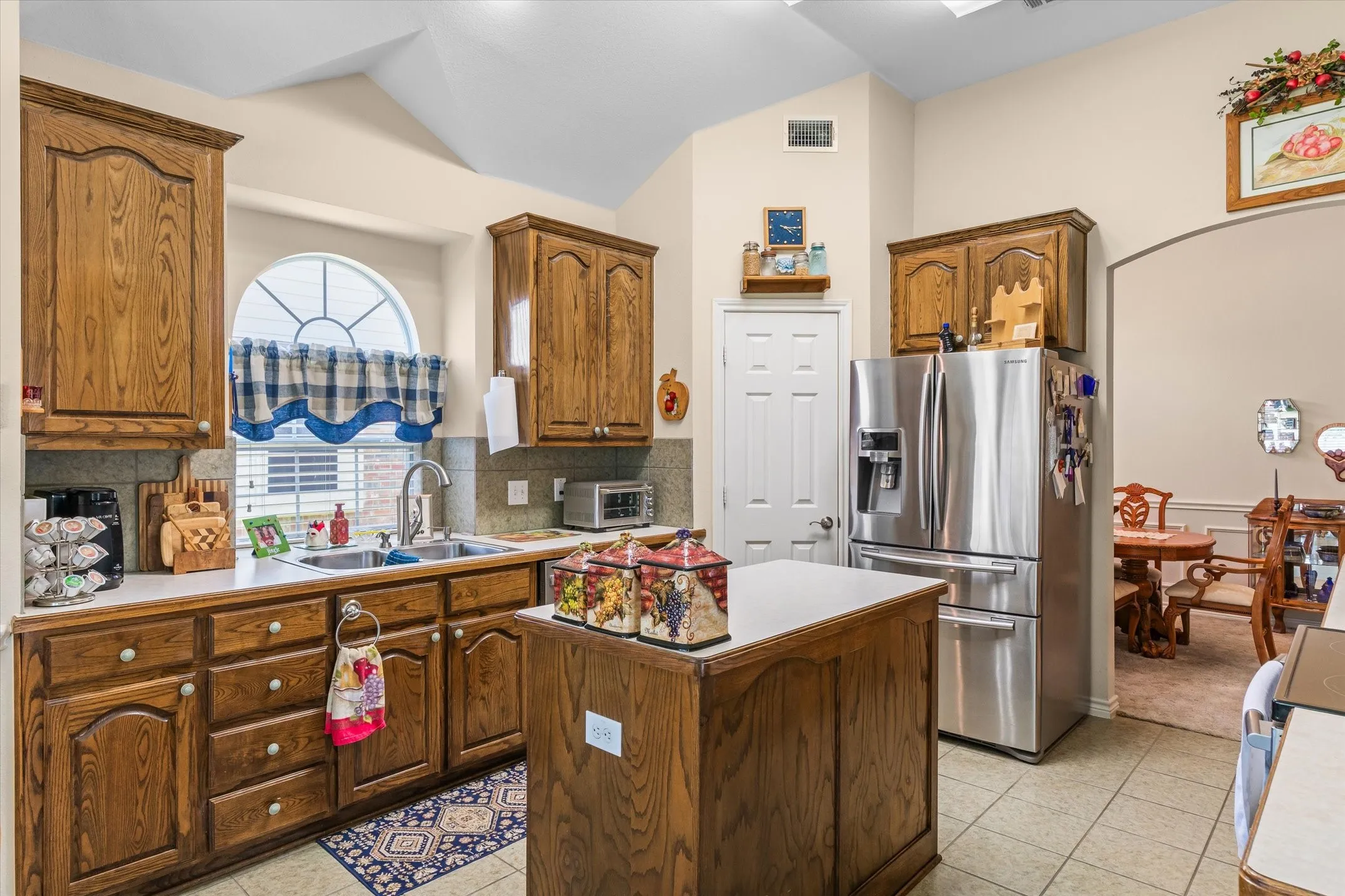 Kitchen featuring wood cabinetry, a central island, tile flooring, and a stainless steel refrigerator