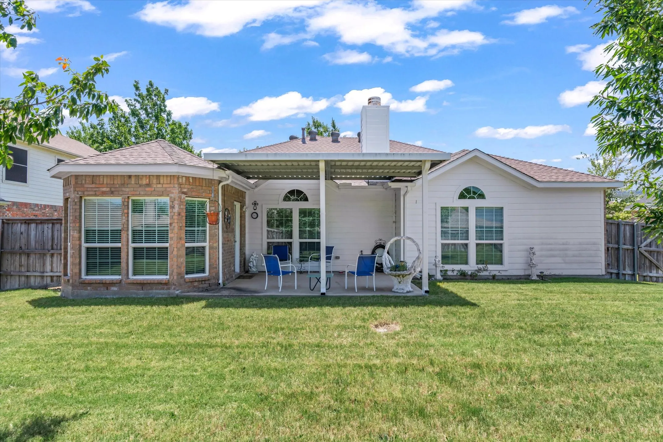 Expansive backyard featuring a covered patio, brick sunroom, durable fencing, and an arched window