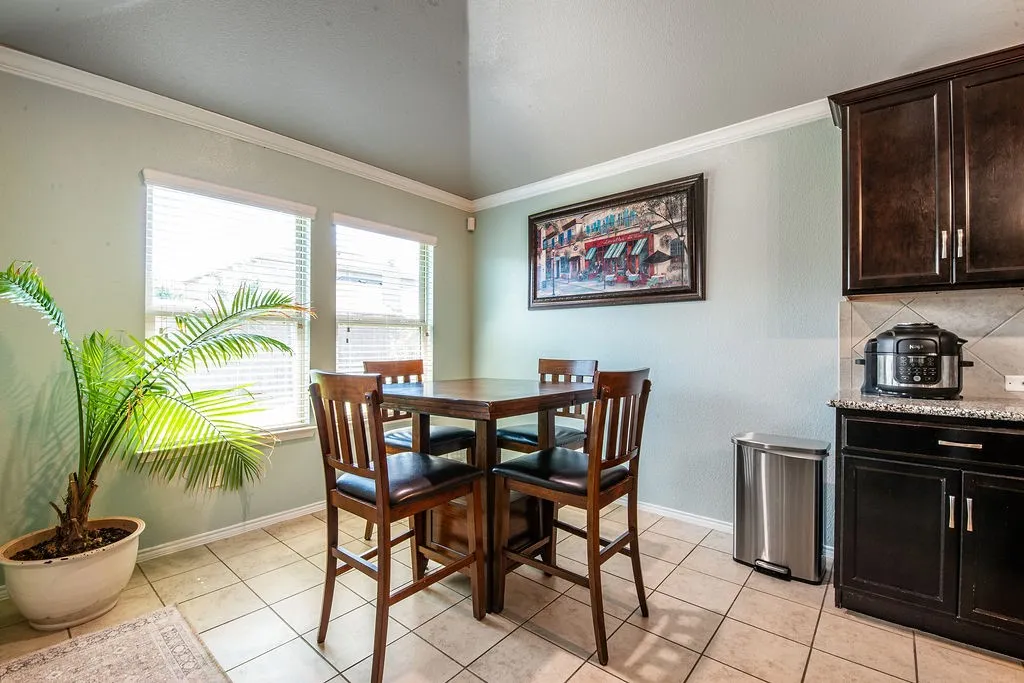 Kitchen dining area featuring tile flooring, dual windows with blinds, crown molding, and dark wood cabinetry with stone countertops
