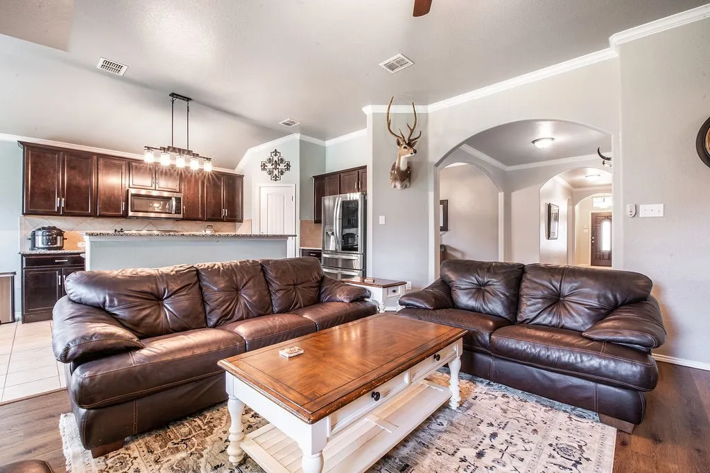 Open-concept living space featuring wood-finish flooring, crown molding, arched doorways, and a ceiling fan
