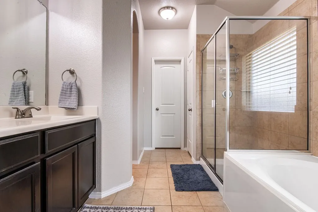 Bathroom featuring a glass-enclosed shower, a separate bathtub, a vanity with a built-in sink, dark wood-finish cabinetry, and beige tile flooring