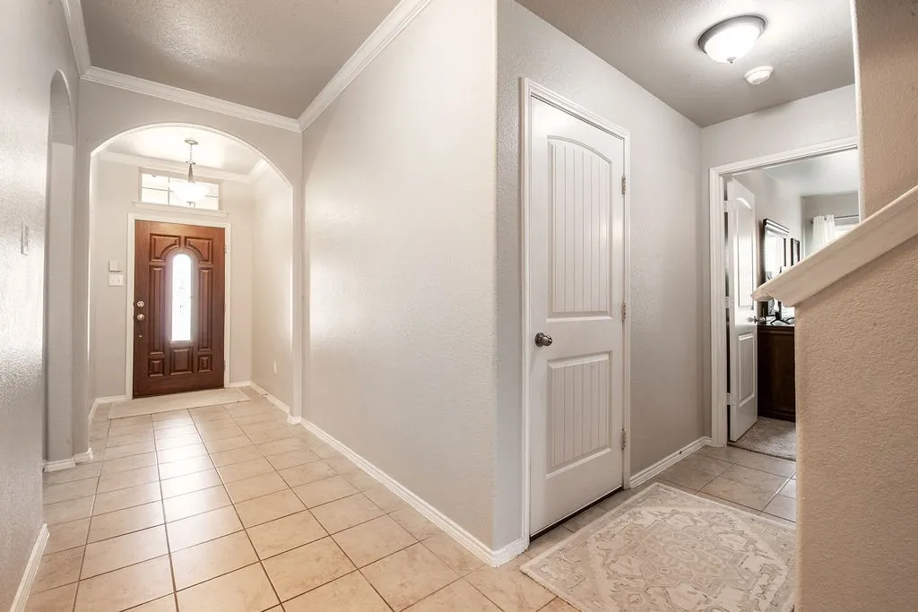 Foyer featuring tile flooring, an arched entryway, a dark wood front door with frosted glass, and crown molding