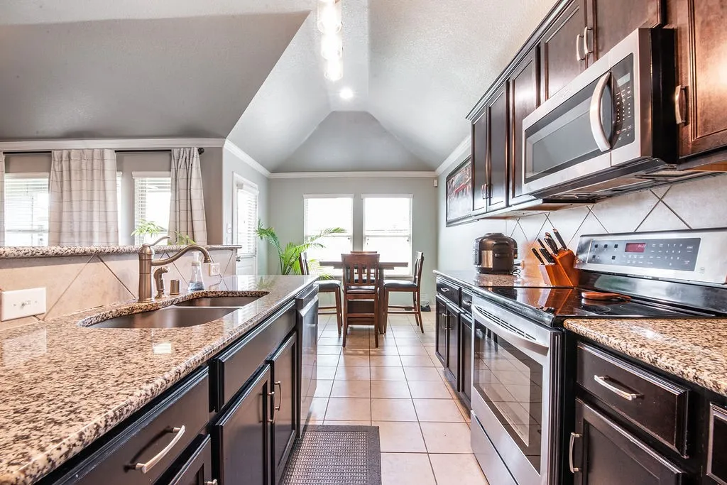 Kitchen featuring granite countertops, dark wood-finish cabinetry, stainless steel appliances, and a tiled backsplash