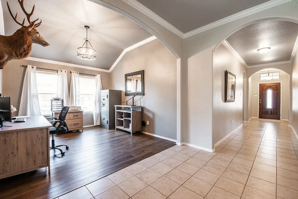 Hallway featuring light-toned square tile flooring leading to a dark wood entry door with an arched transom window