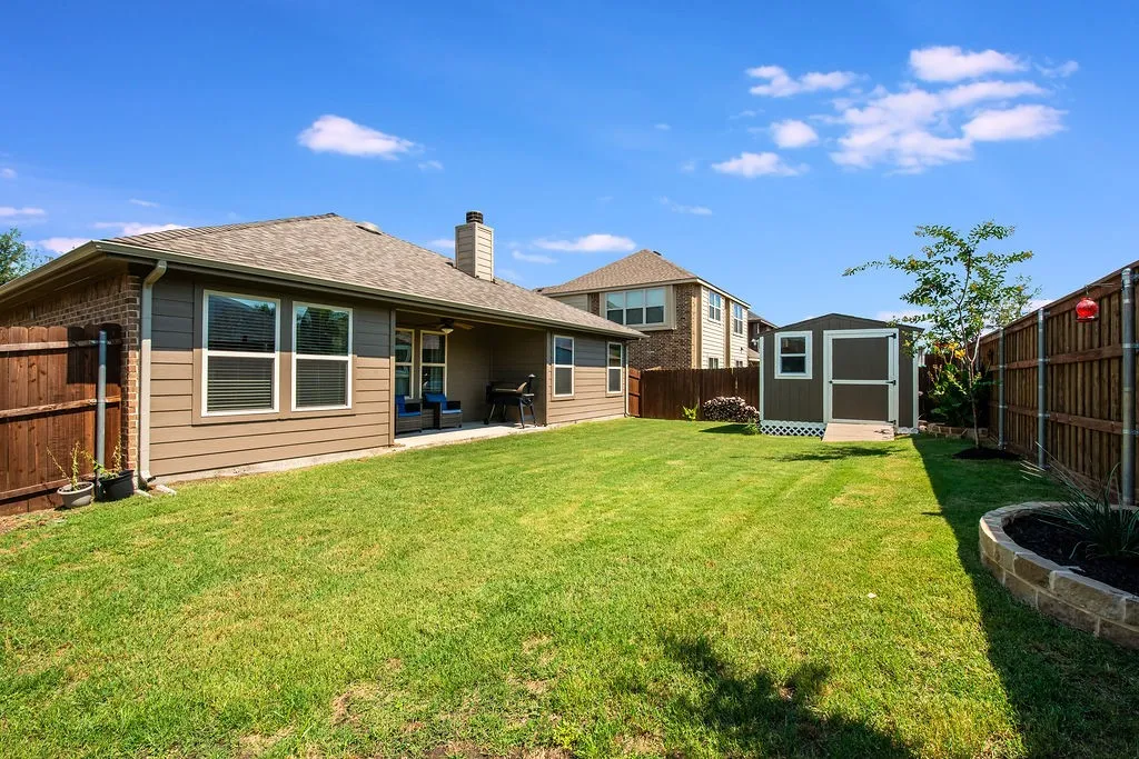 Expansive backyard featuring a manicured lawn, a detached storage shed, a stone-edged planting bed, and a privacy fence