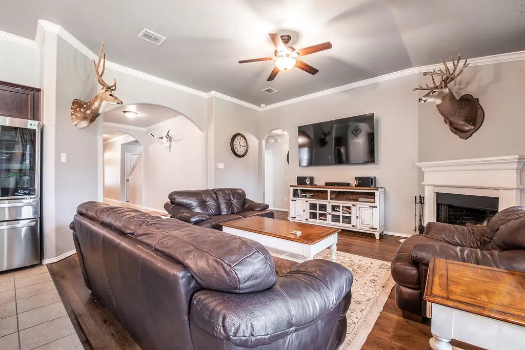 Living area featuring wood-finish flooring, a fireplace with a white mantel, and ceiling fan