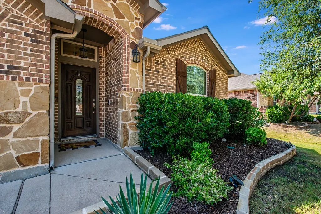 Brick and stone facade featuring a dark wood entry door with decorative glass insert, arched entryway, and sconce lighting