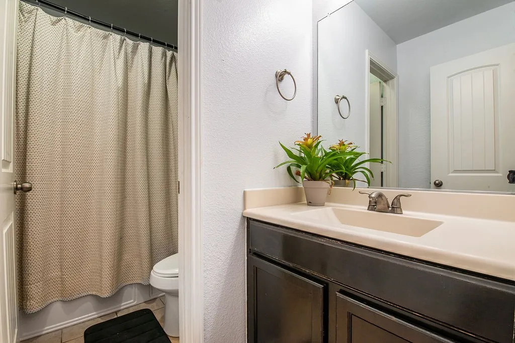 Secondary Bathroom featuring a dark wood-finish vanity with an integrated basin, a large wall mirror, and brushed nickel fixtures
