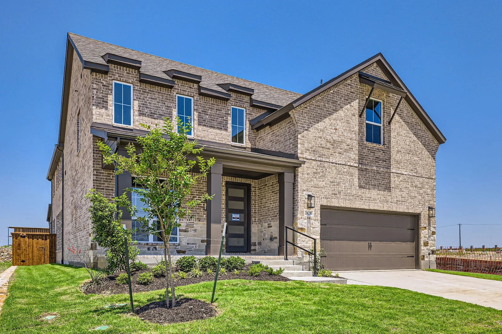 Two-story brick exterior with stone accents, a covered front porch, and a two-car garage