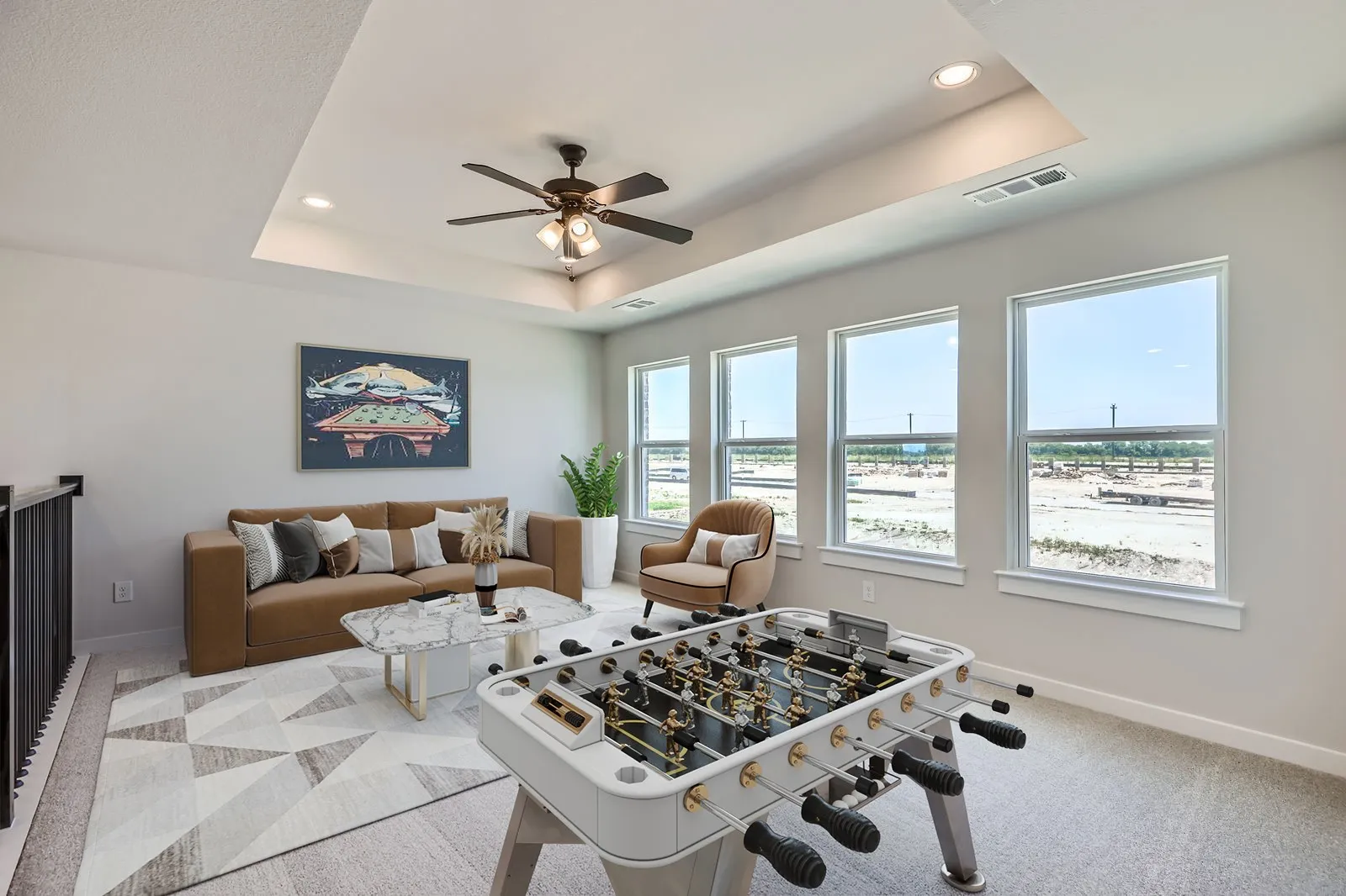 Spacious loft area featuring a tray ceiling with recessed lighting and a ceiling fan, multiple windows, light-toned carpeting, and a black metal railing