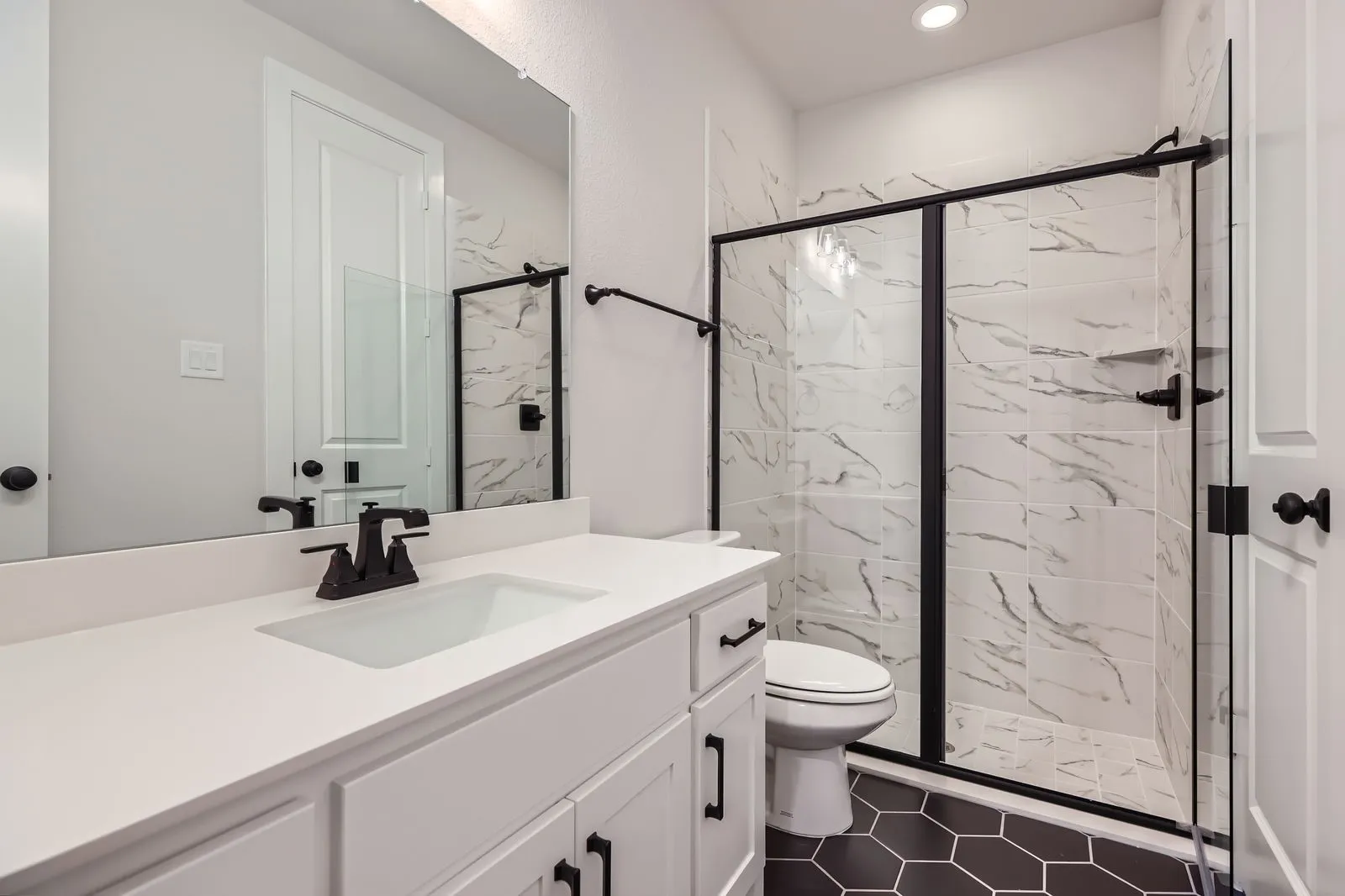 Bathroom featuring a white vanity with integrated sink and matte black faucet, a large frameless mirror, and a shower with black-framed glass enclosure and marble-look tile surround