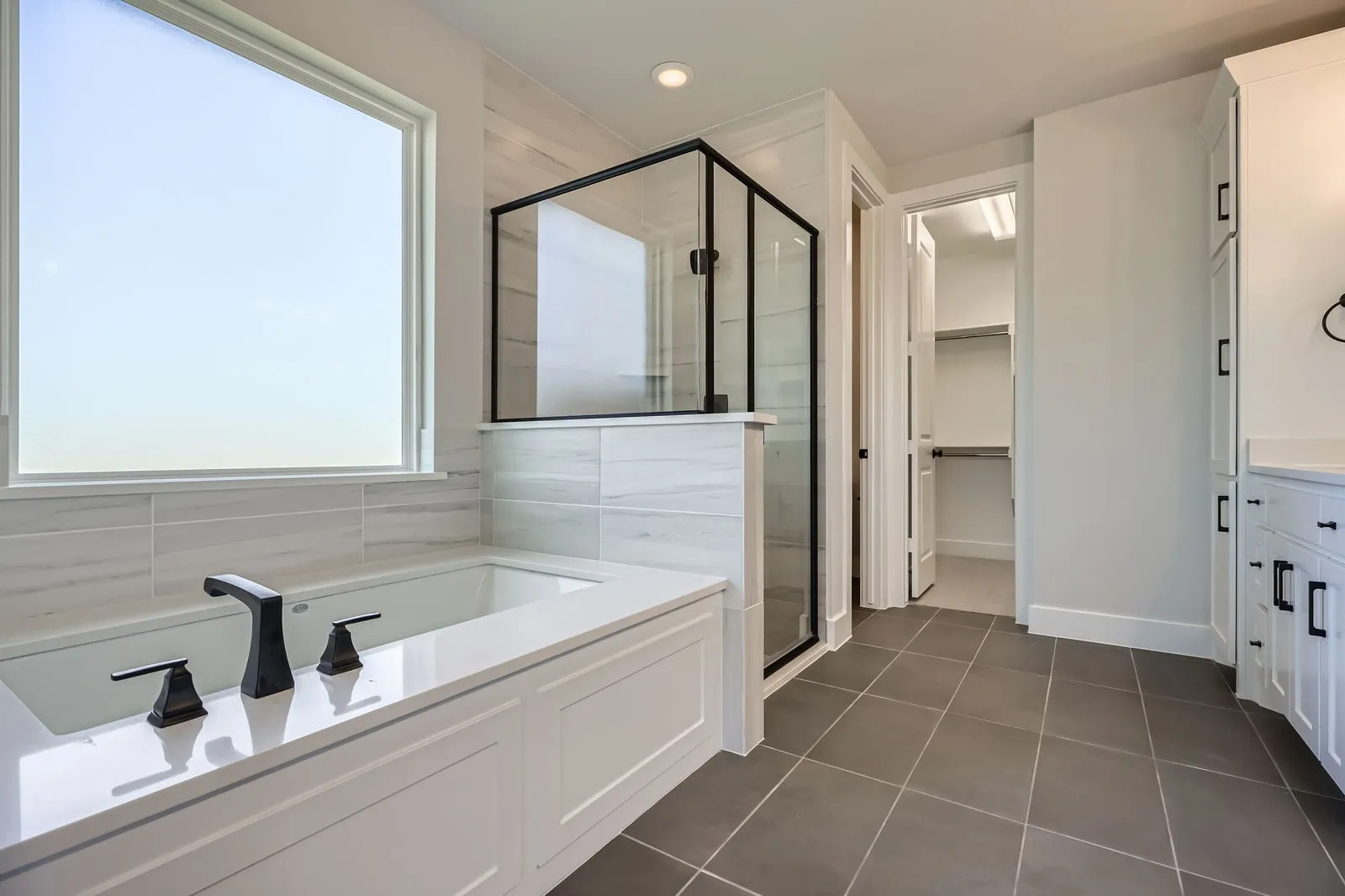Soaking tub with a quartz surround and matte black fixtures, set against a tiled wall