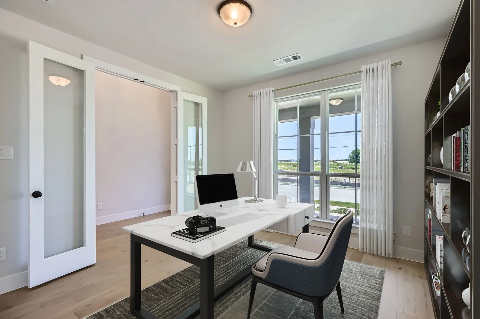 Dedicated interior space featuring wood-finish flooring, a large window, a built-in bookshelf, and sliding double doors with glass panels