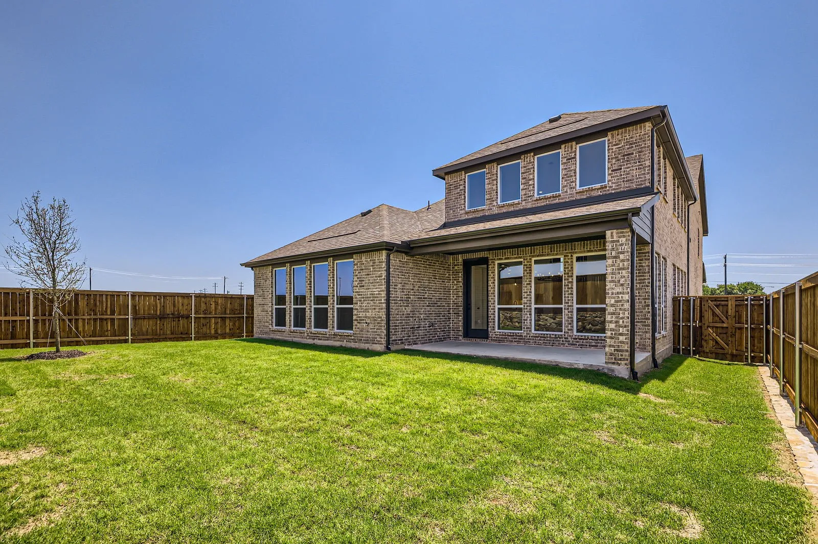 Spacious backyard featuring a covered patio, extensive lawn, full privacy fencing, and a mature tree