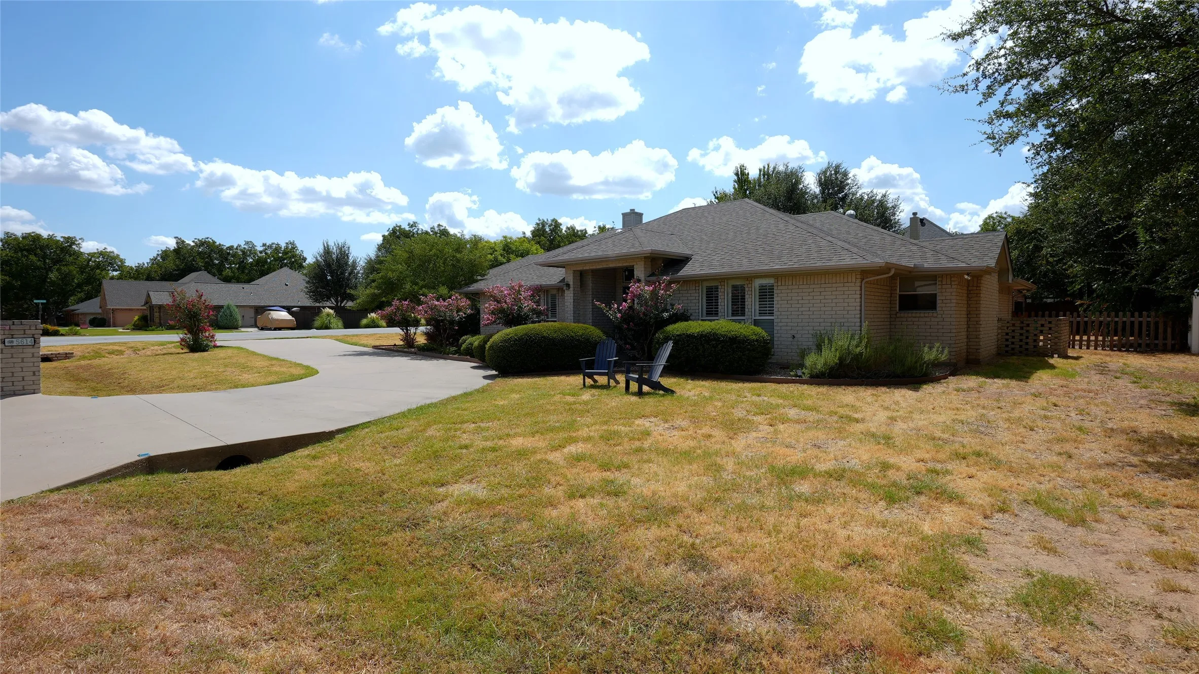 Brick exterior with a shingle roof, mature landscaping, and an attached privacy fence