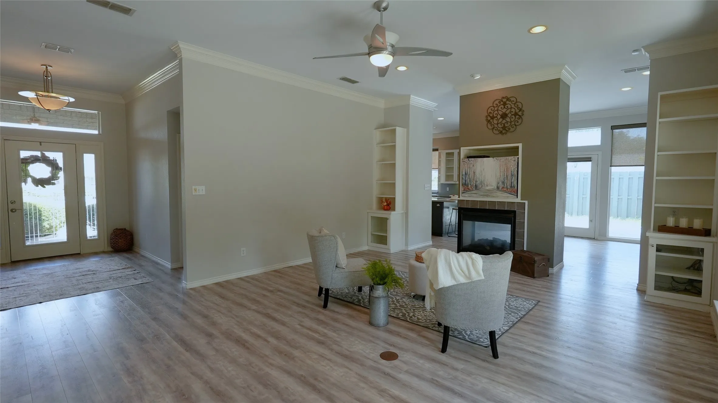 Wood-finish flooring throughout, featuring a fireplace with a dark brick surround, white built-in shelving, an entry door with sidelights, and crown molding