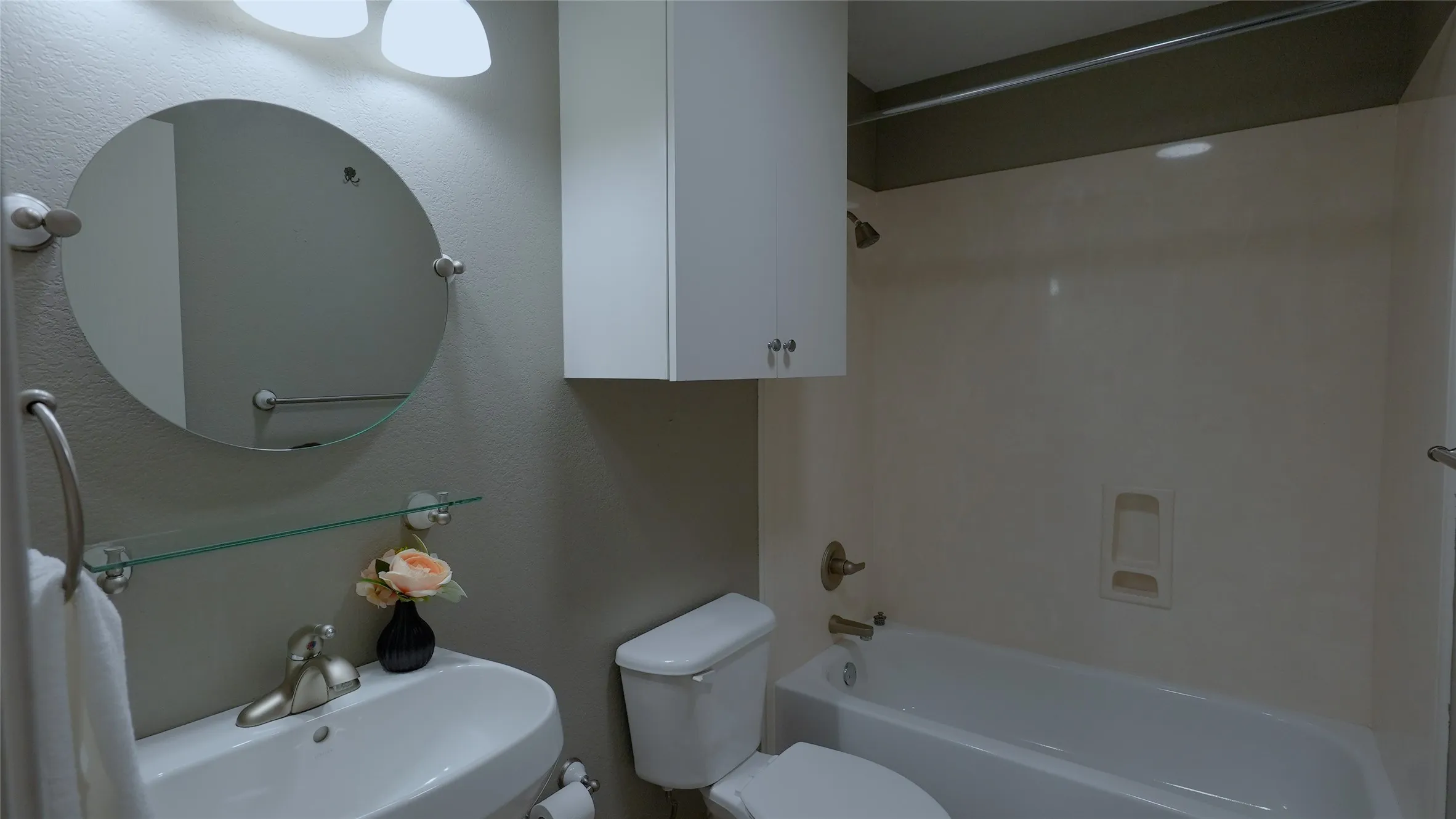 White vanity with an integrated sink, a circular mirror, and a glass shelf