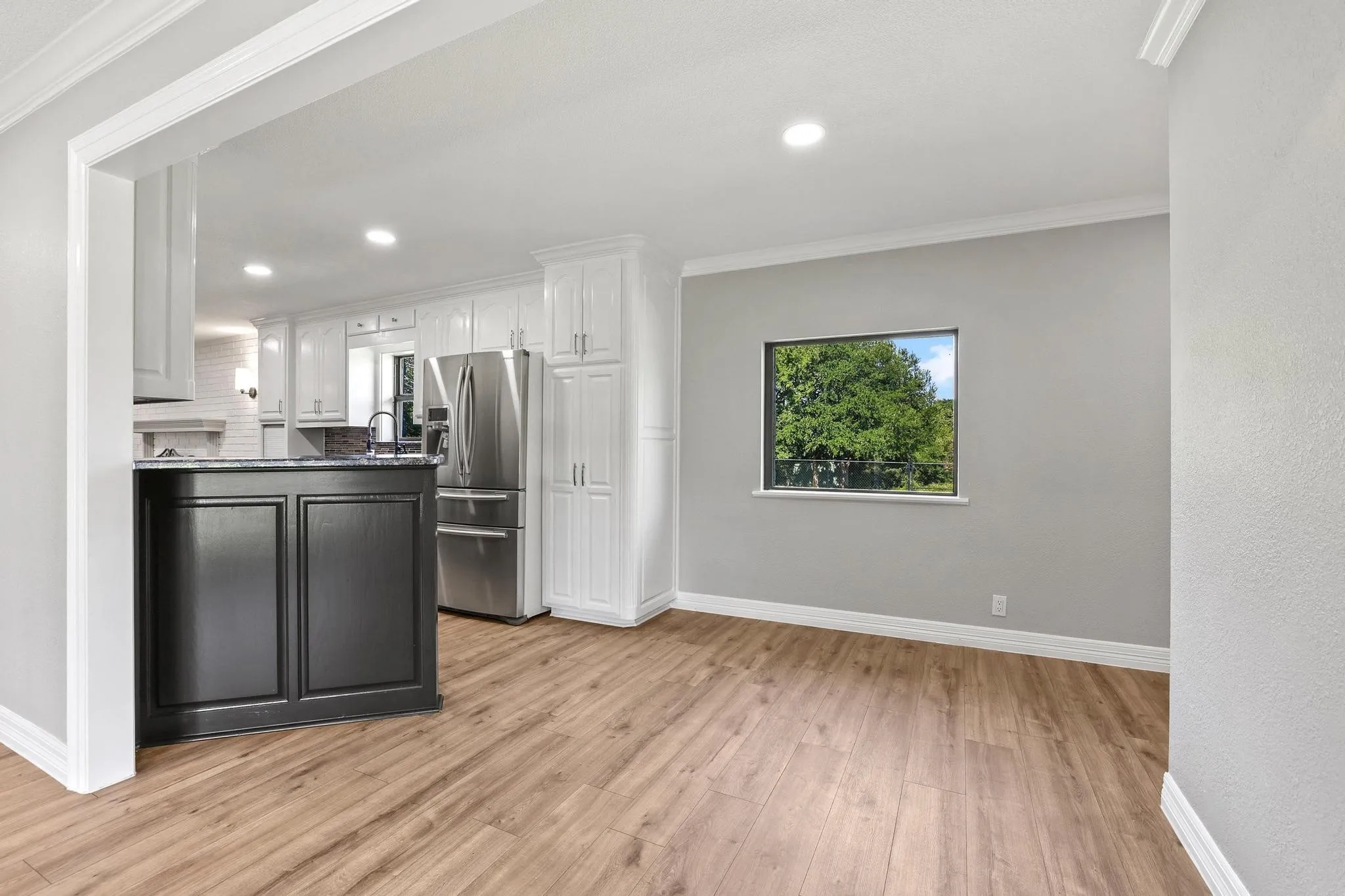 Kitchen and living area featuring wood-finish flooring, white crown molding, and recessed lighting