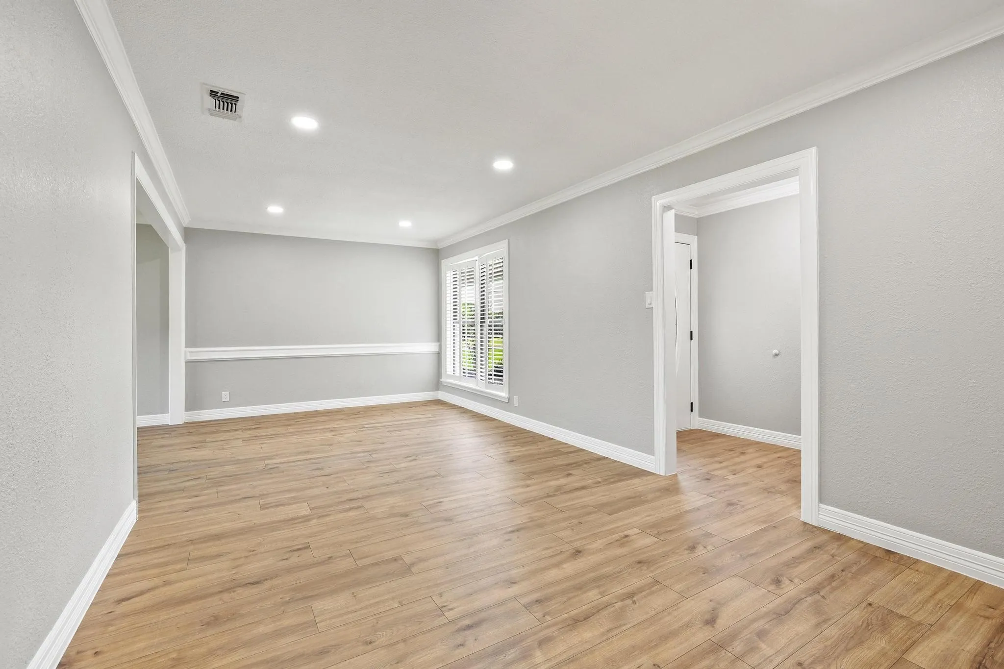 Spacious interior featuring wood-finish flooring, recessed lighting, crown molding, and a window with blinds