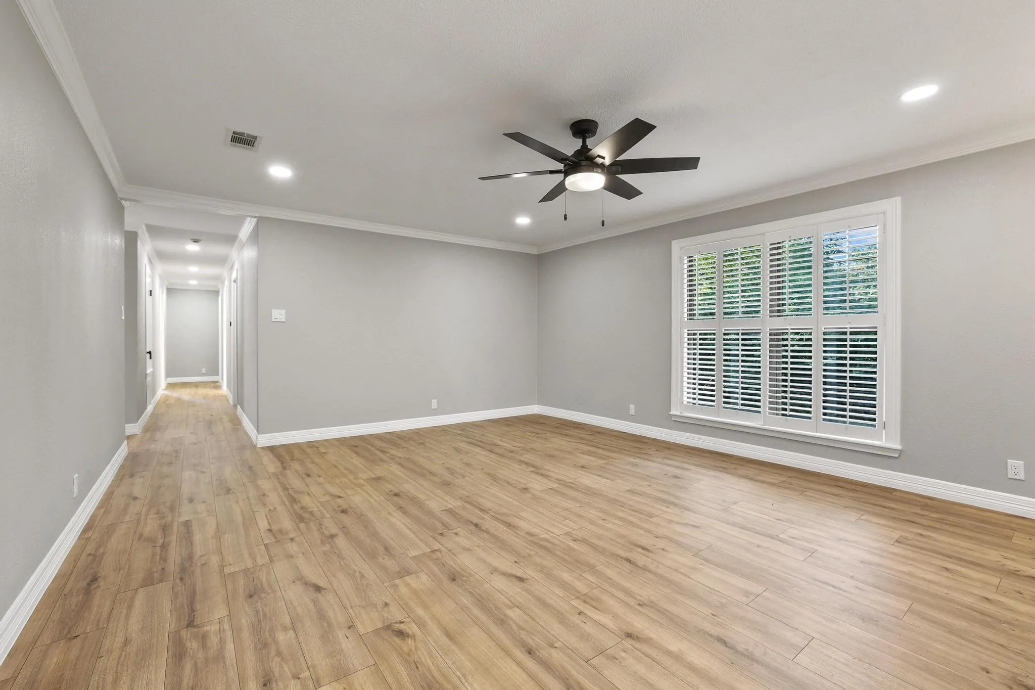 Spacious room featuring wood-finish flooring, light grey walls, and white crown molding