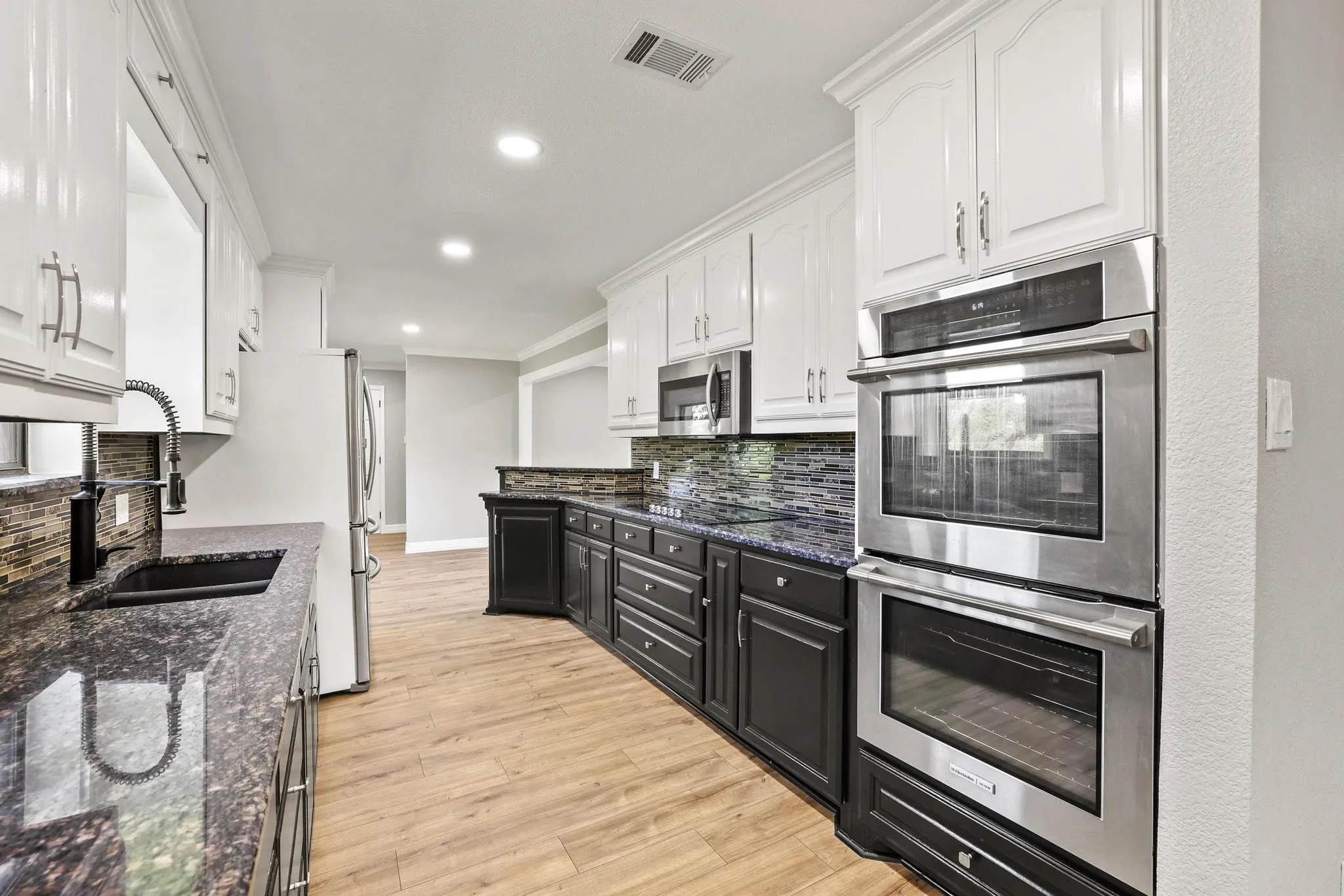 Kitchen featuring wood-finish flooring, two-tone cabinetry with white upper and dark lower cabinets, granite countertops, and stainless steel double ovens