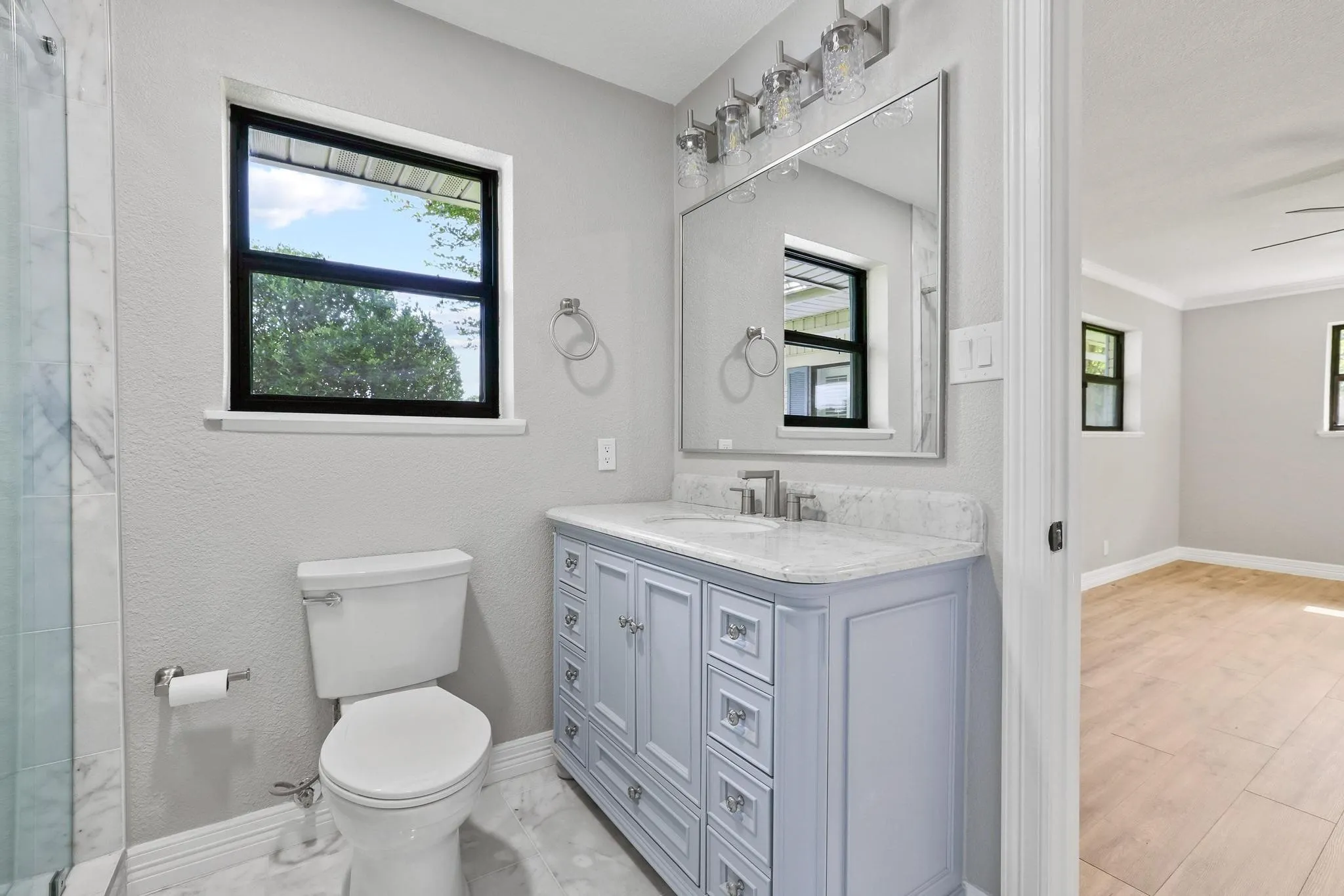Bathroom featuring a light blue vanity with a stone countertop, a rectangular undermount sink, and a framed mirror with a four-bulb vanity light fixture
