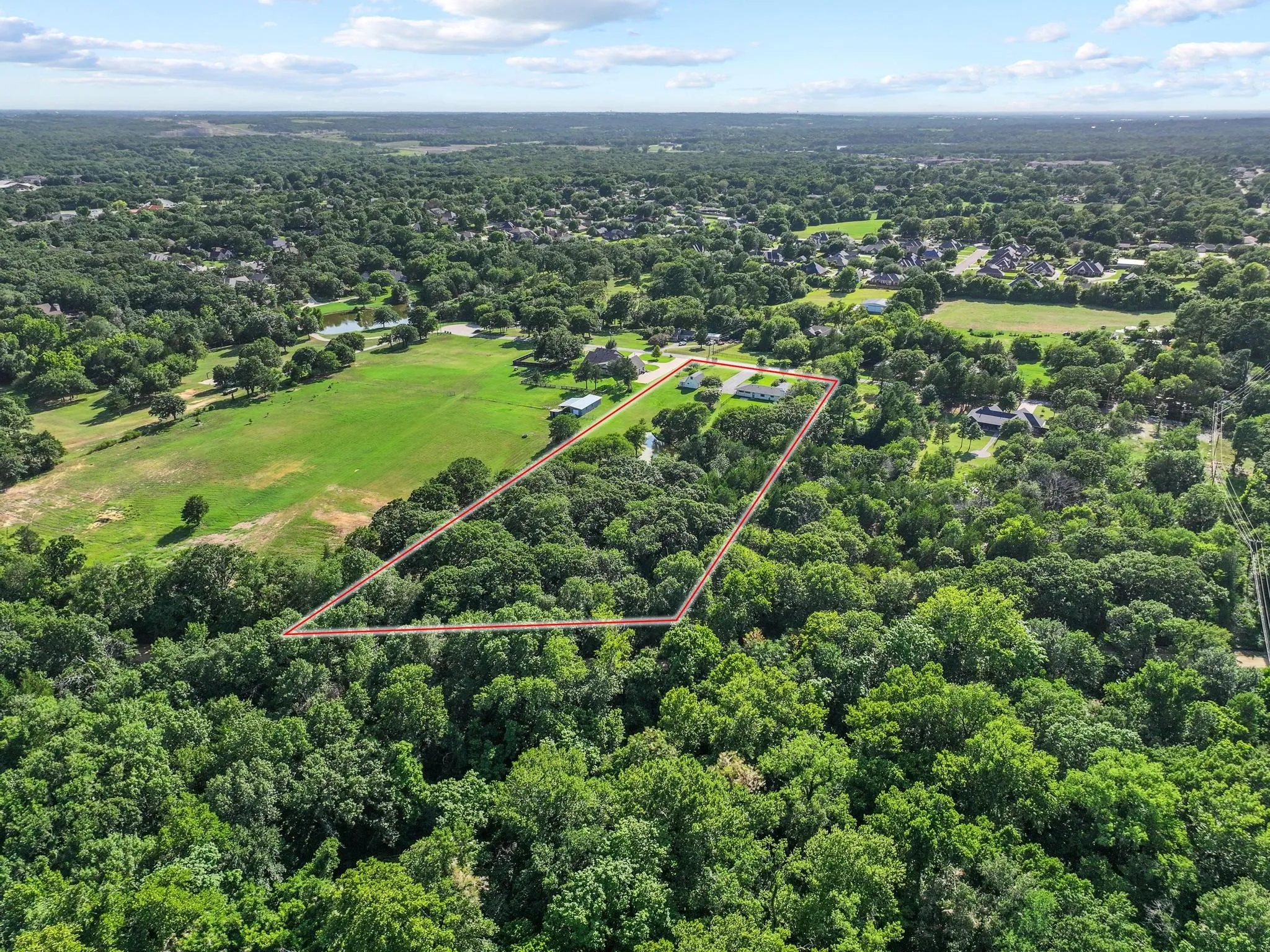 Expansive parcel featuring mature trees, a defined property boundary, and distant structures