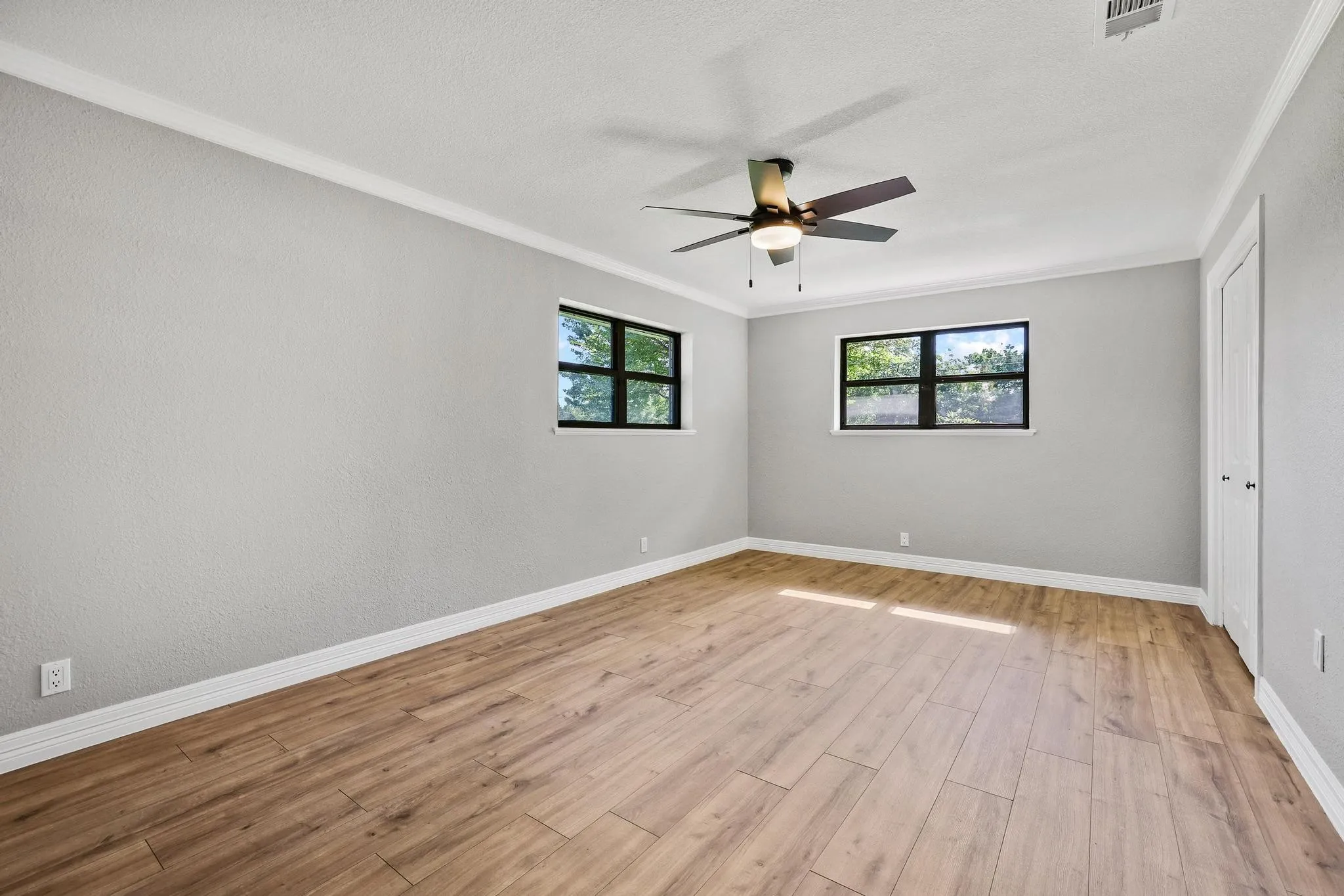 Spacious room featuring wood-finish flooring, light grey walls, and white crown molding