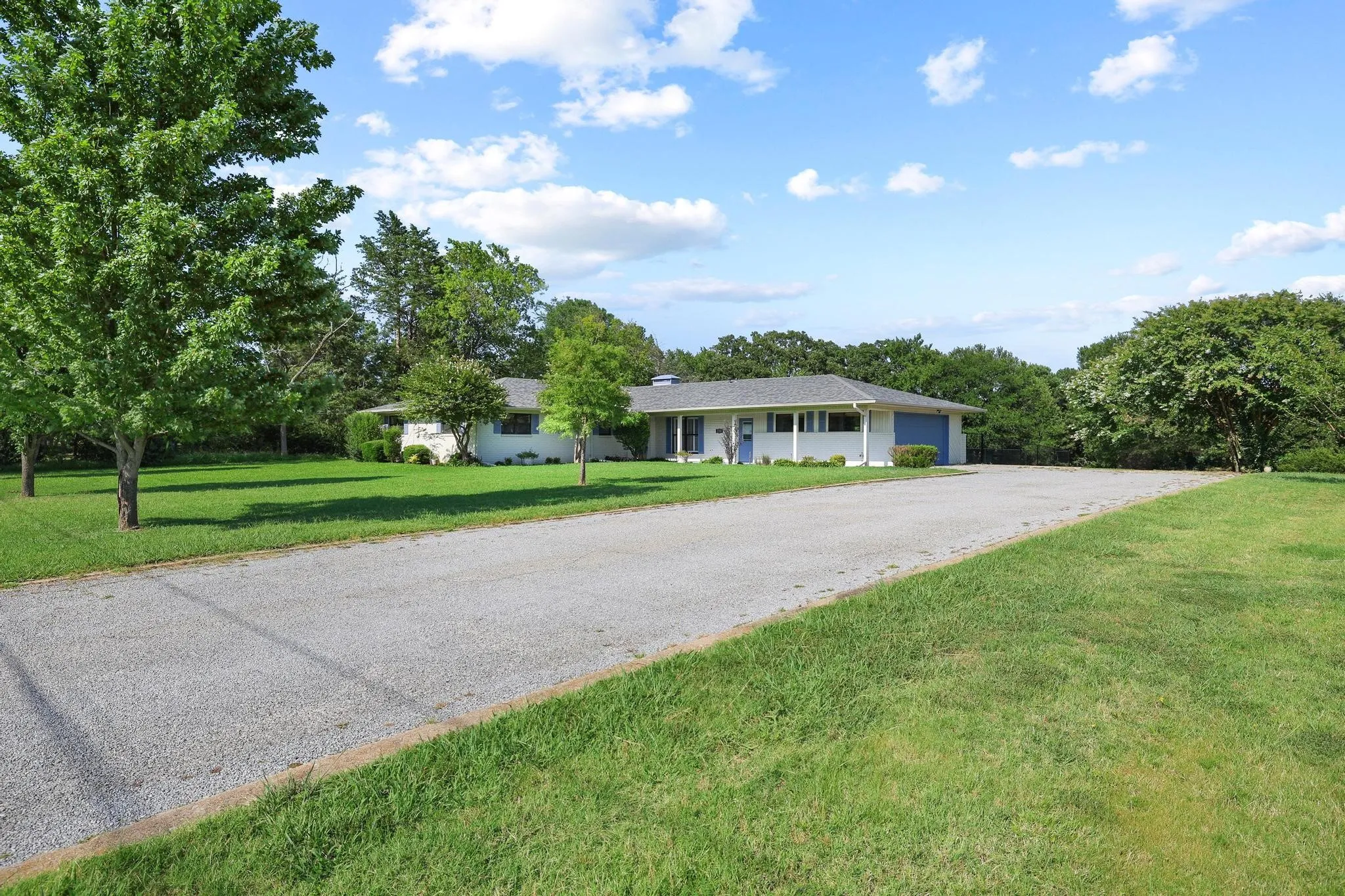 Single-story residence featuring a gravel driveway, white exterior siding, and a contrasting blue garage door