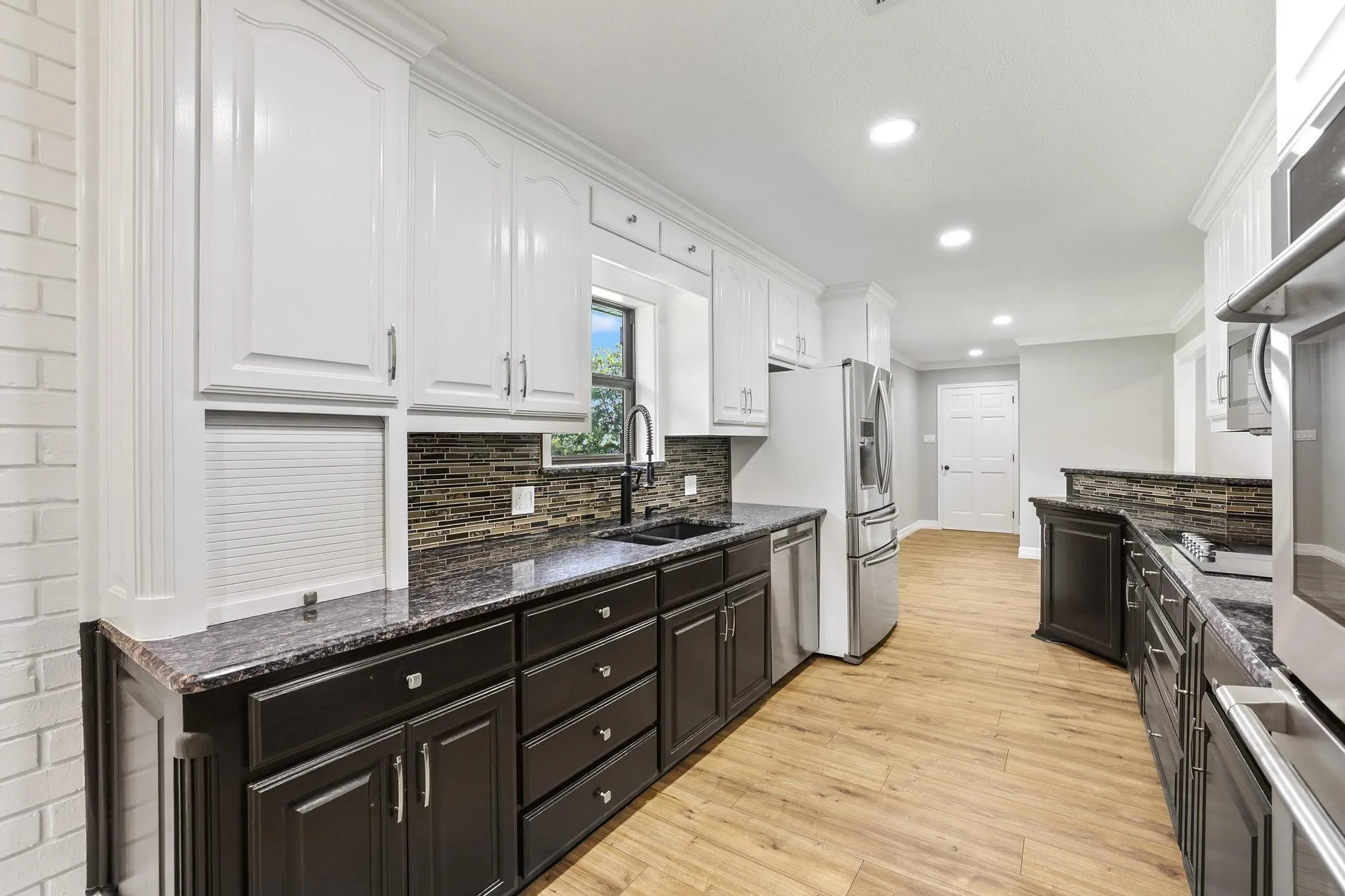 Kitchen featuring light wood-finish flooring, white upper cabinetry, dark lower cabinetry, dark countertops, and a mosaic tile backsplash