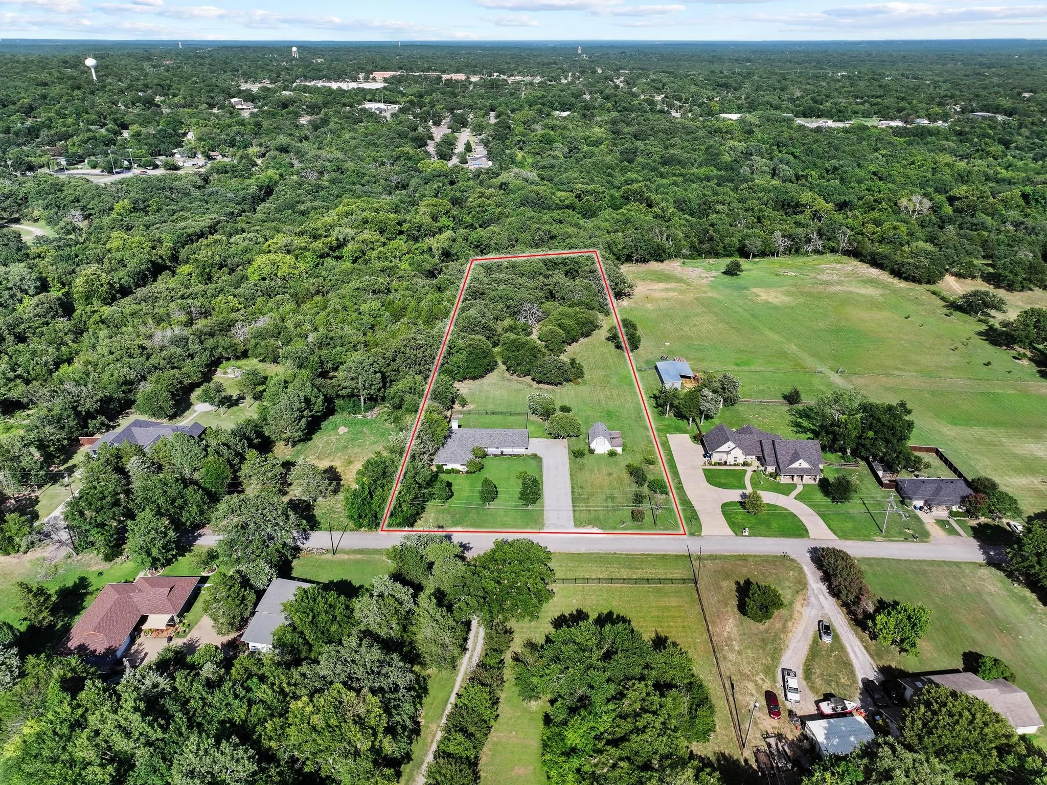 Expansive property featuring a single-story residence with a light-toned roof, a paved driveway, and mature trees