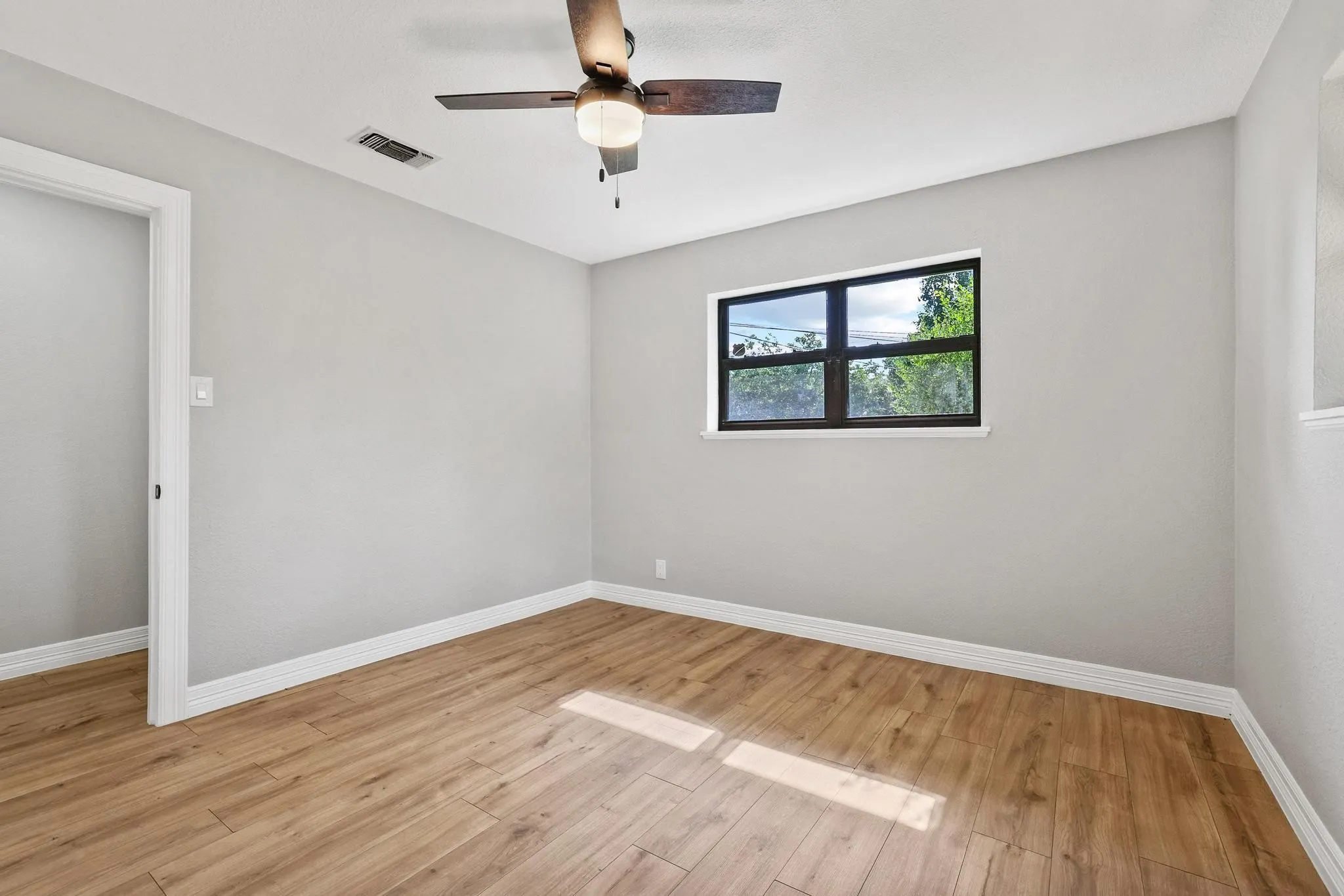 Light-filled room featuring wood-finish flooring, a ceiling fan with integrated lighting, a dark-framed window, and neutral wall paint