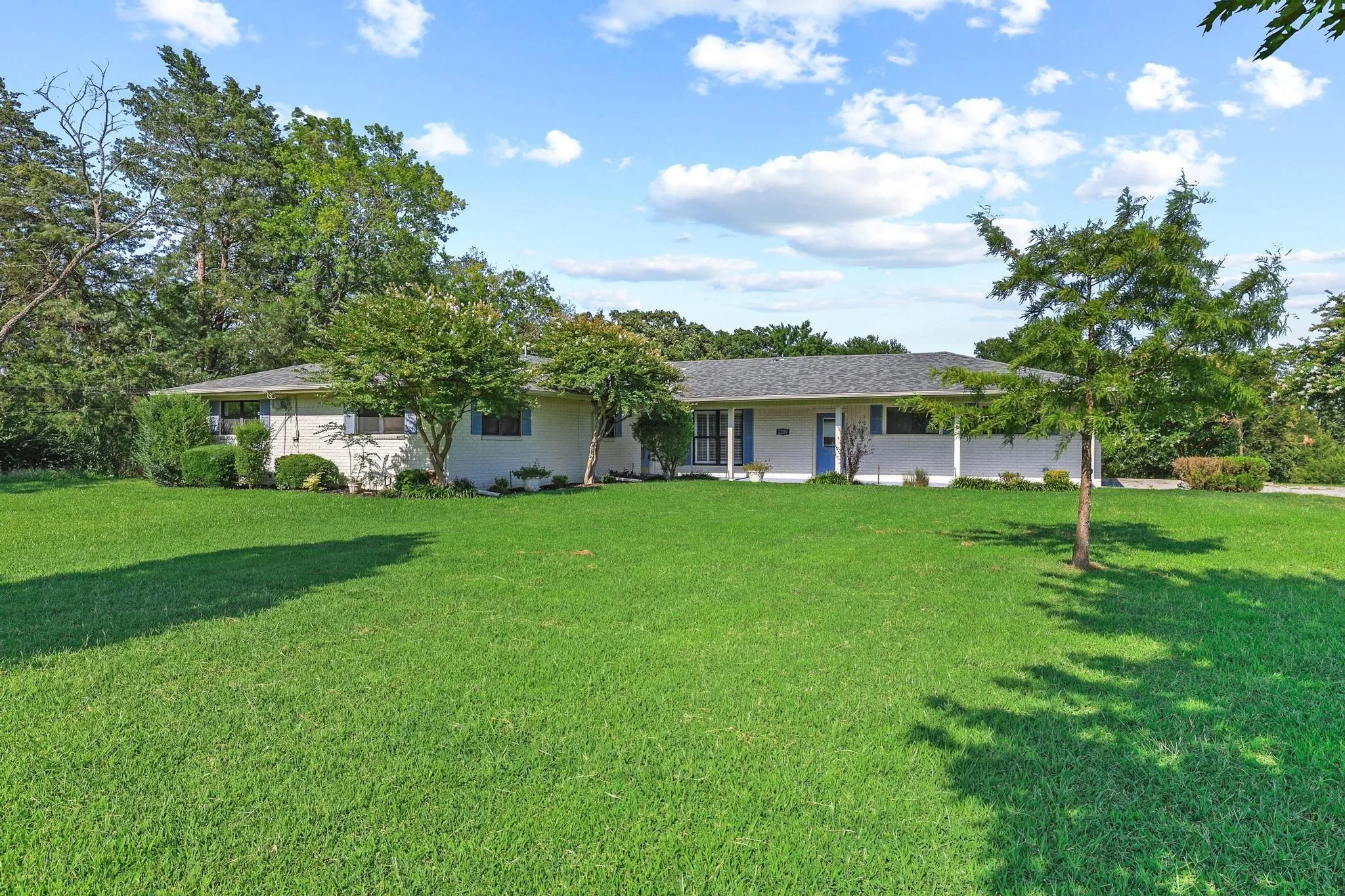 Expansive front lawn with mature trees and landscaped shrubbery