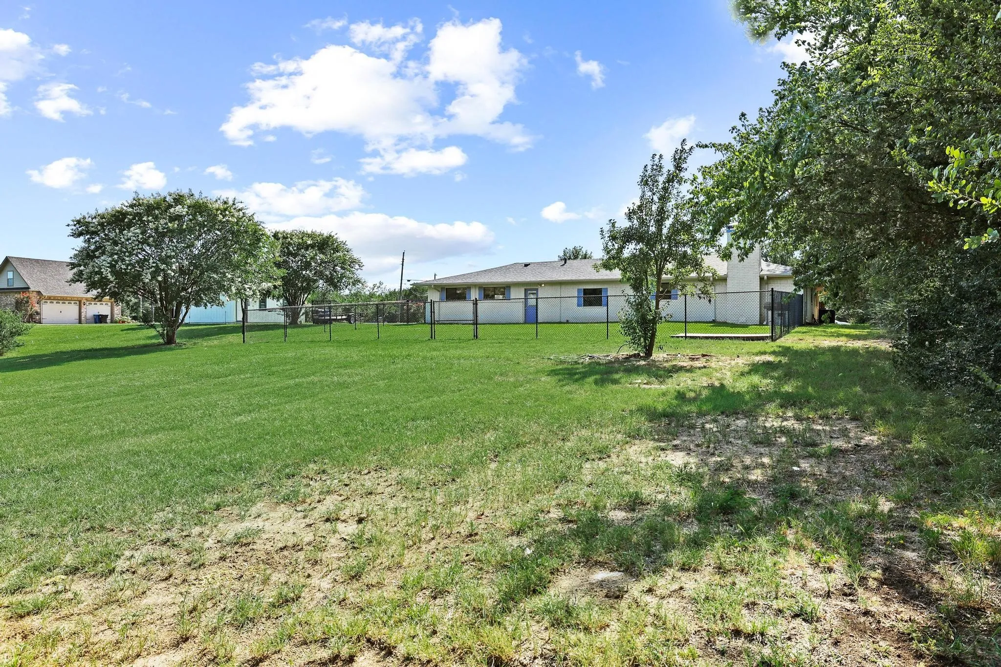 Expansive fenced yard featuring a well-maintained lawn and mature trees