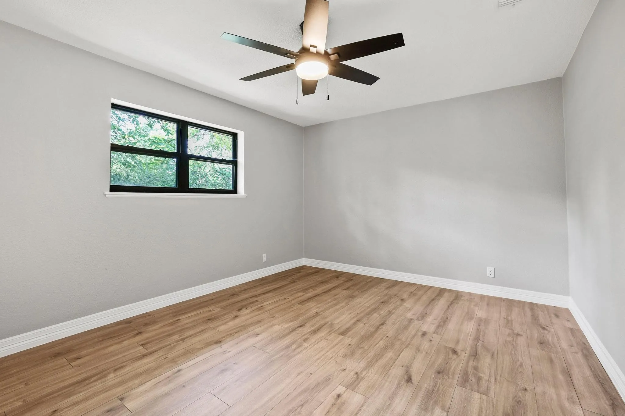 Spacious room featuring wood-finish flooring, light grey walls, and a contemporary ceiling fan with integrated lighting